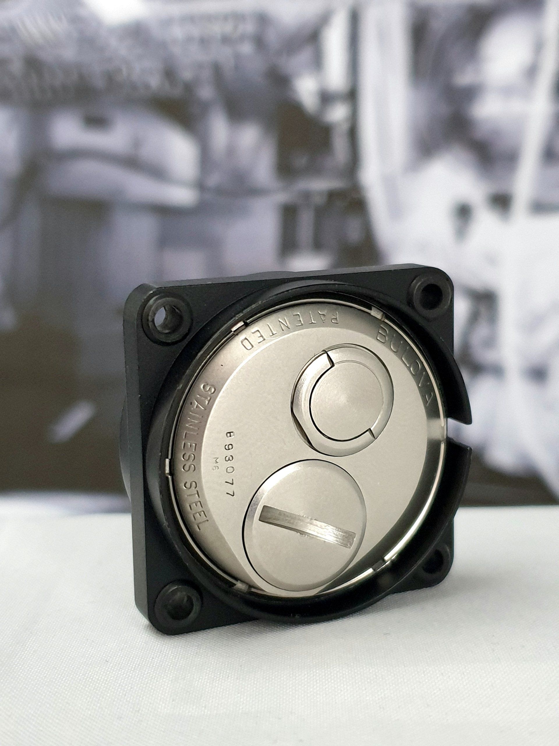 Small black electronic device with a silver circular dial on a tabletop, blurred background