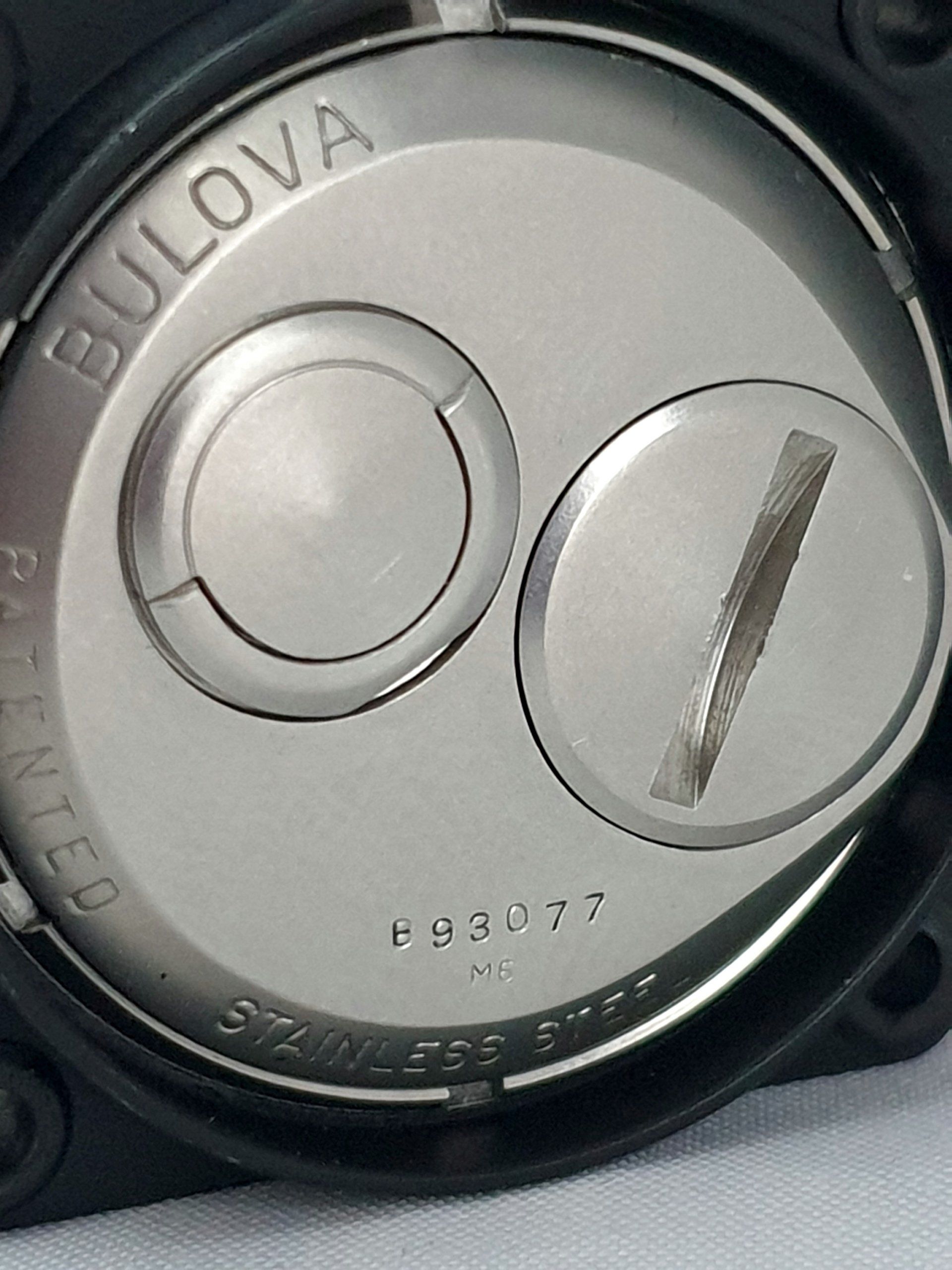 Close-up of a silver Bulova watch case back with engraved text and two circular battery covers.