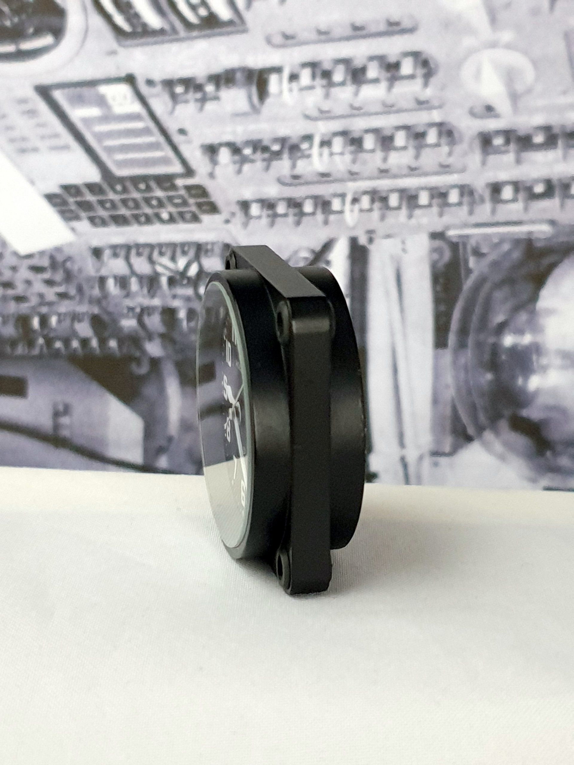 Black wireless earbud resting on a white surface against a blurred black-and-white background.