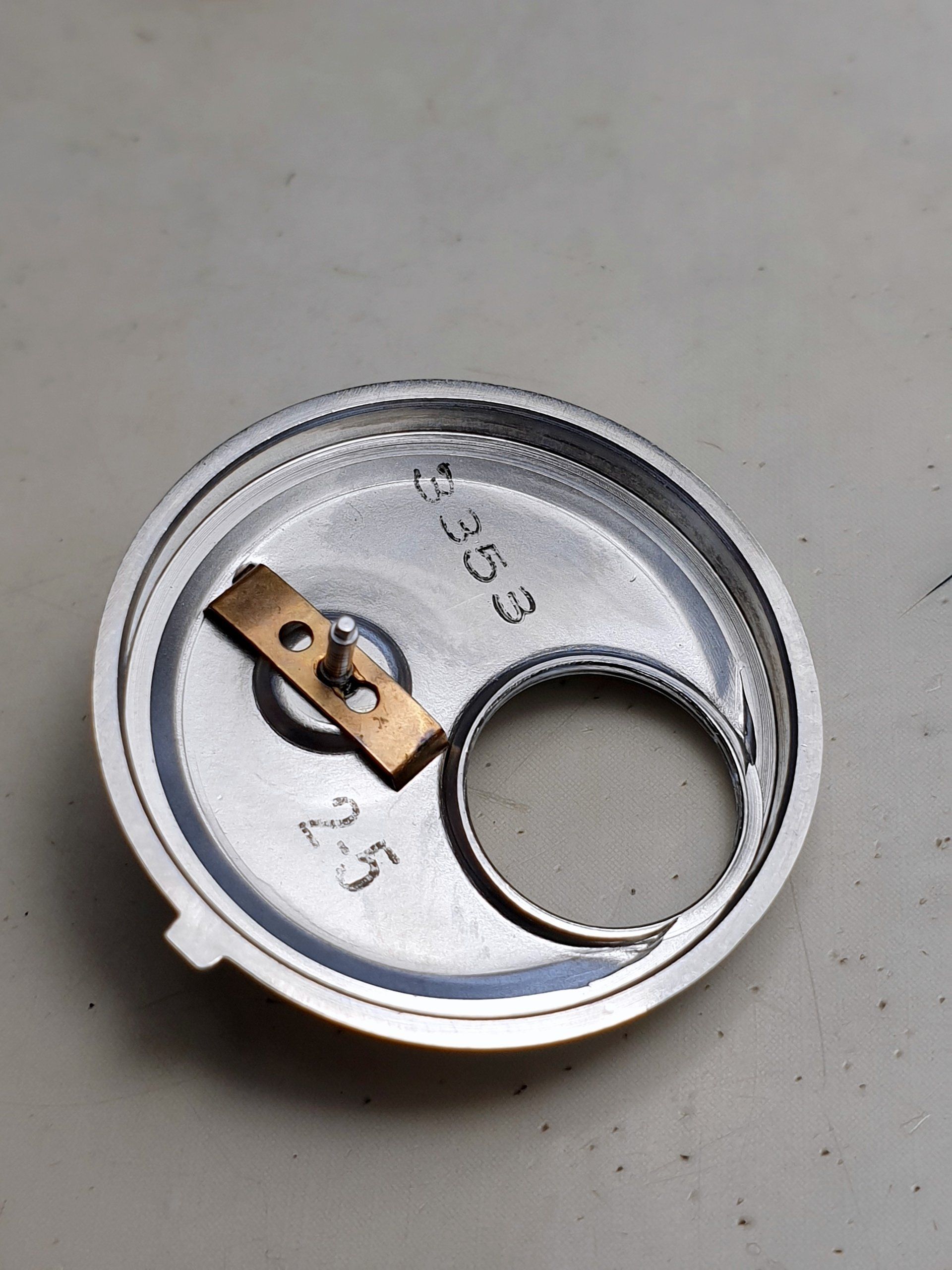 Metal can lid with an attached pull tab on a light gray surface