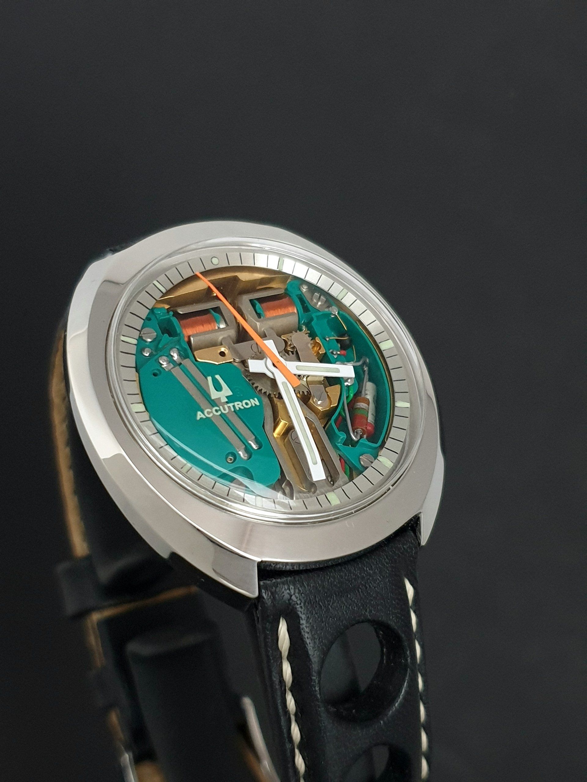 Silver wristwatch with exposed mechanical movement and teal dial on a black leather strap
