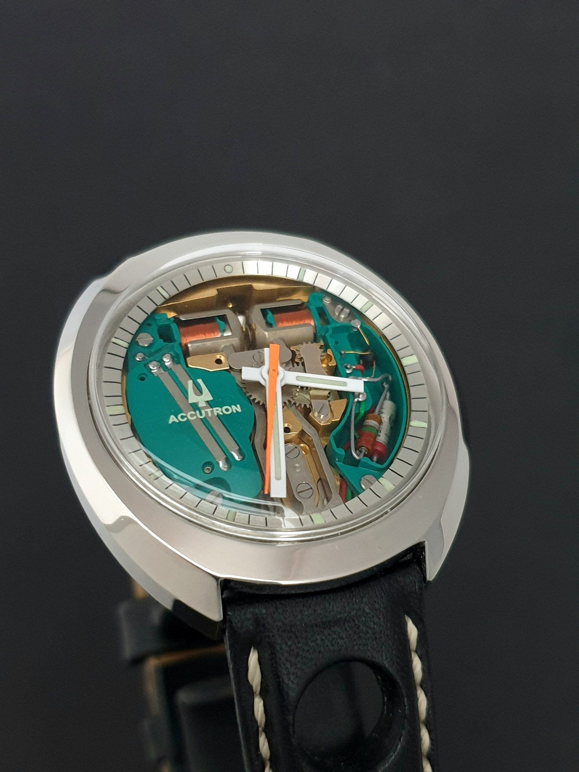 Close-up of a silver watch with a turquoise skeleton dial and black leather strap.