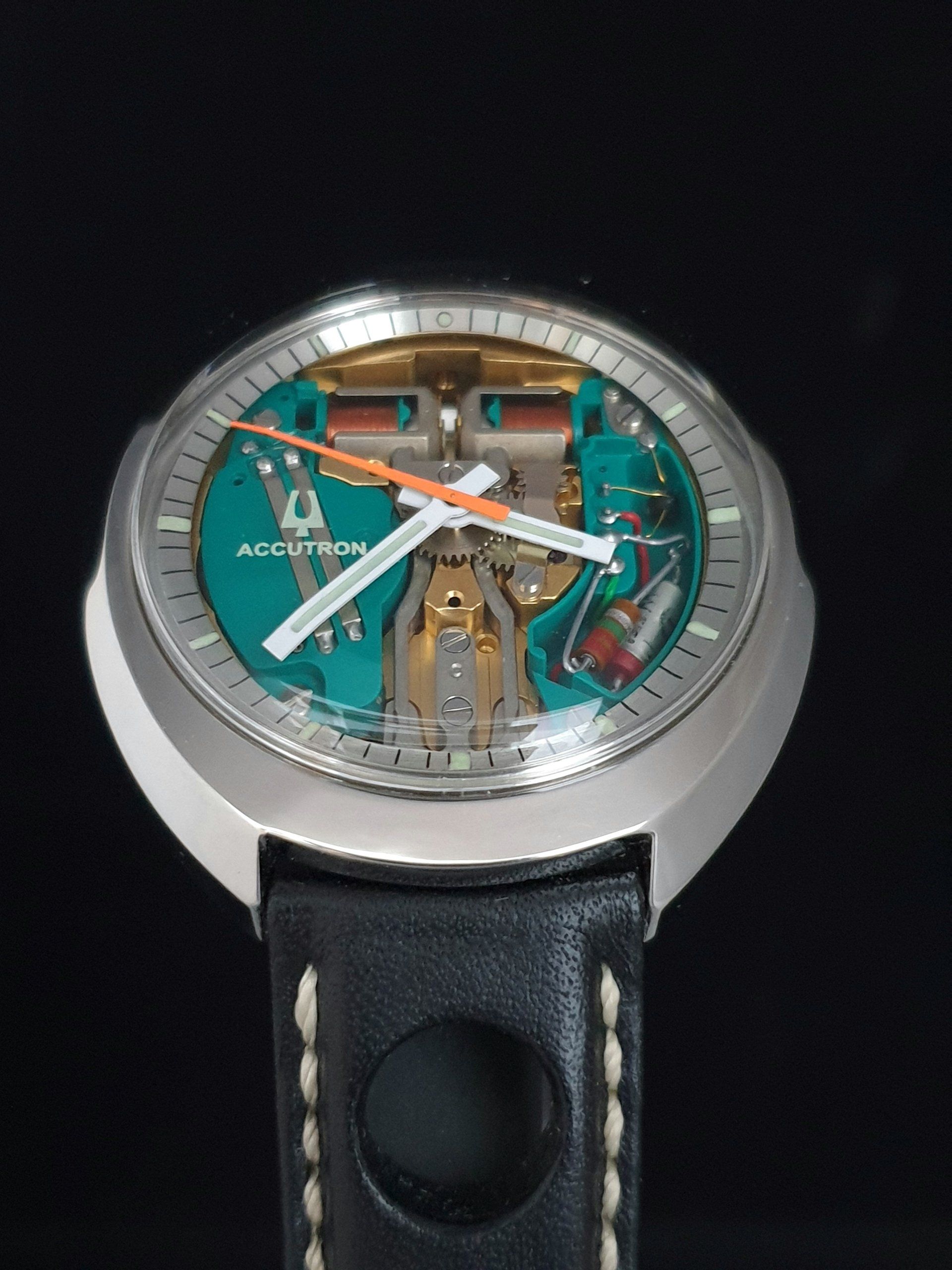 Close-up of a silver skeleton wristwatch with a teal and black dial on a black strap