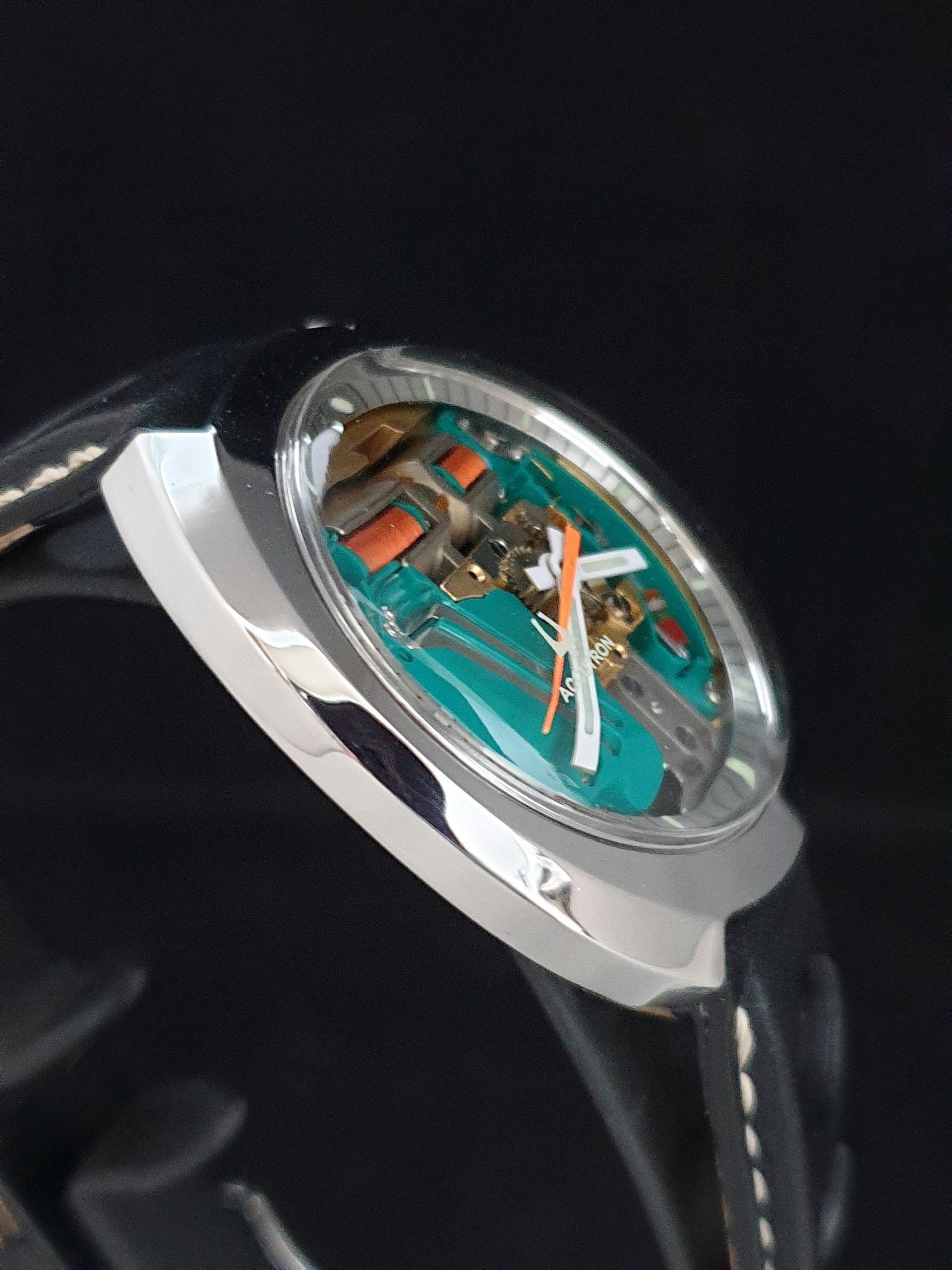 Close-up of a silver wristwatch with a turquoise skeleton dial and black leather strap