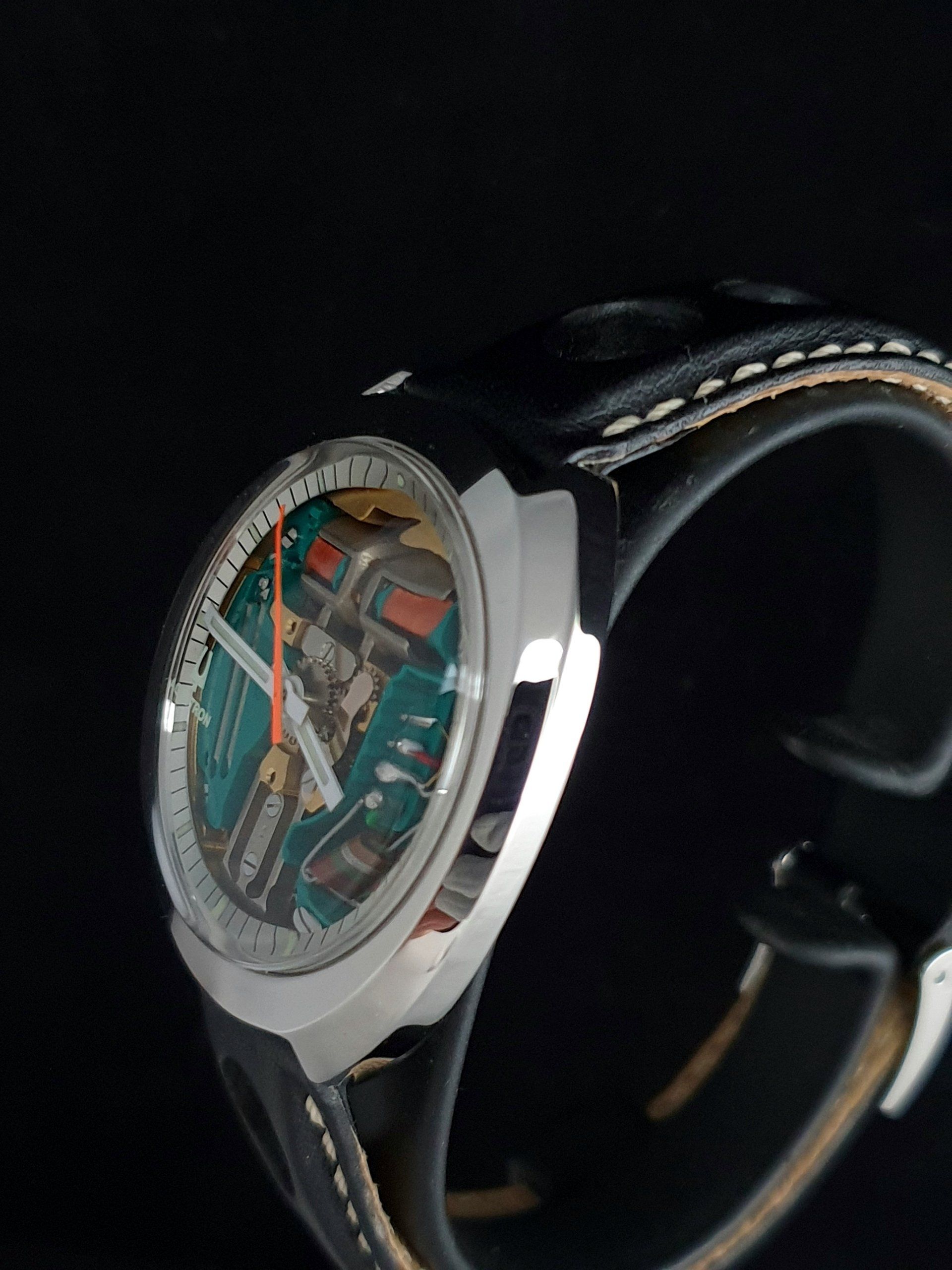 Close-up of a silver wristwatch with a teal dial and black leather strap on a dark background
