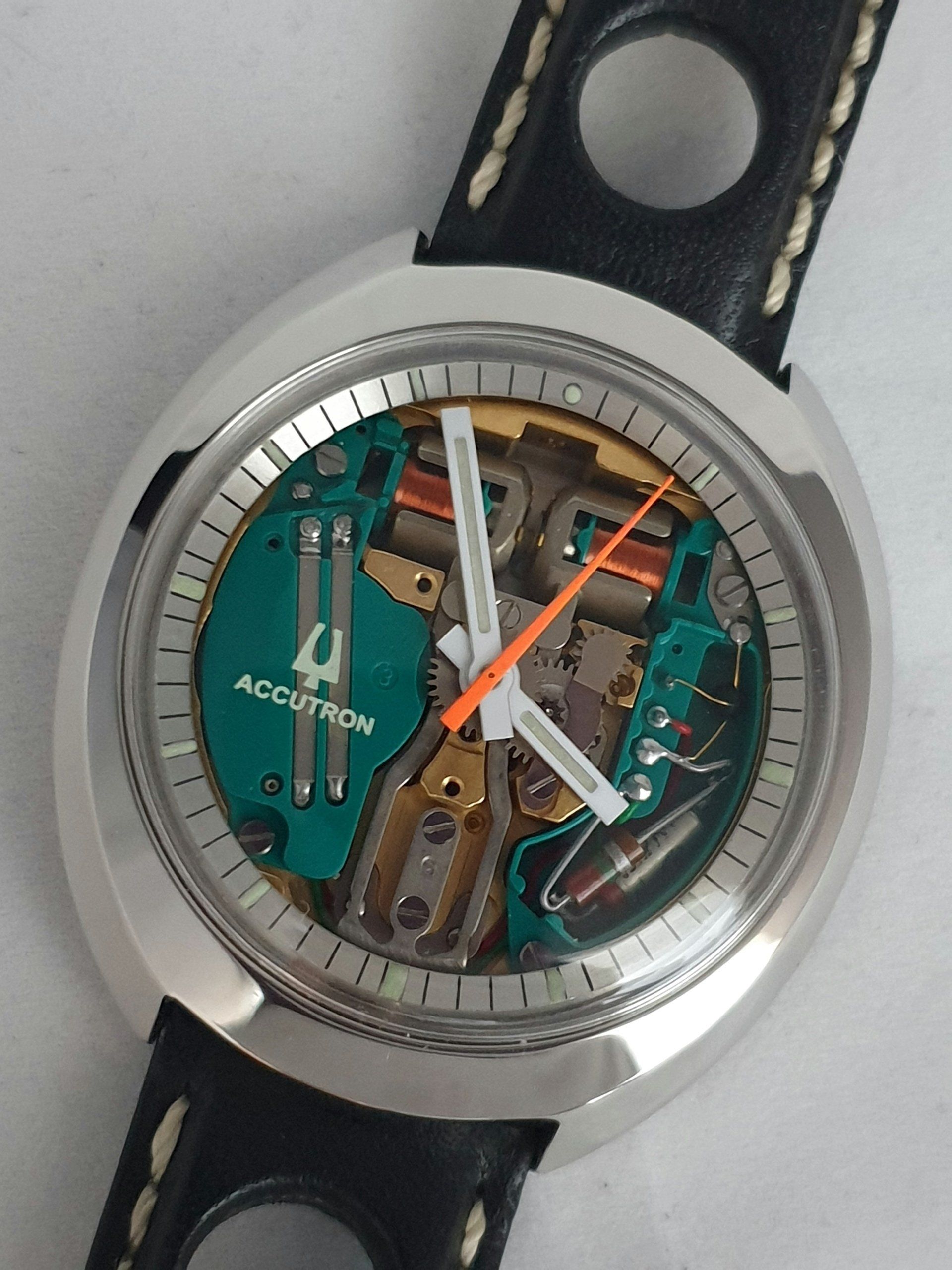 Close-up of a silver wristwatch with a black strap and visible green mechanical movement underneath.