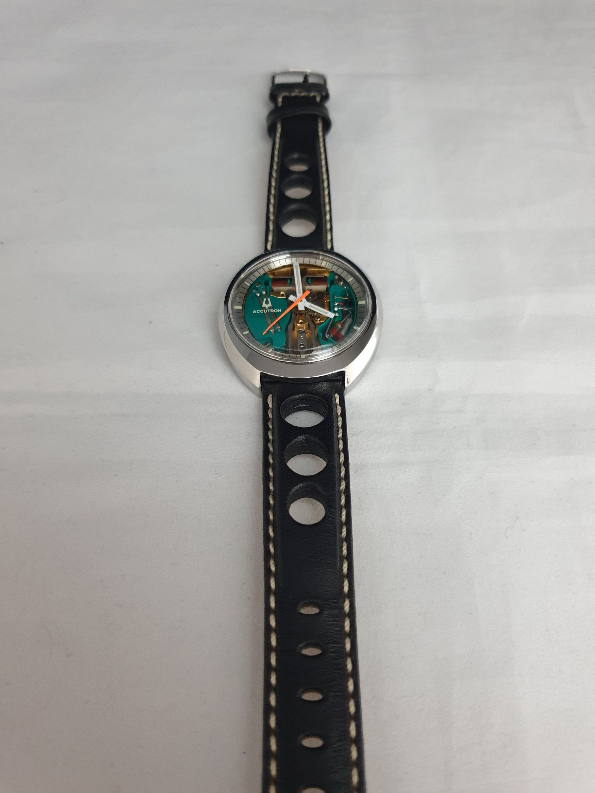 Silver watch with green dial and black perforated strap on a white surface