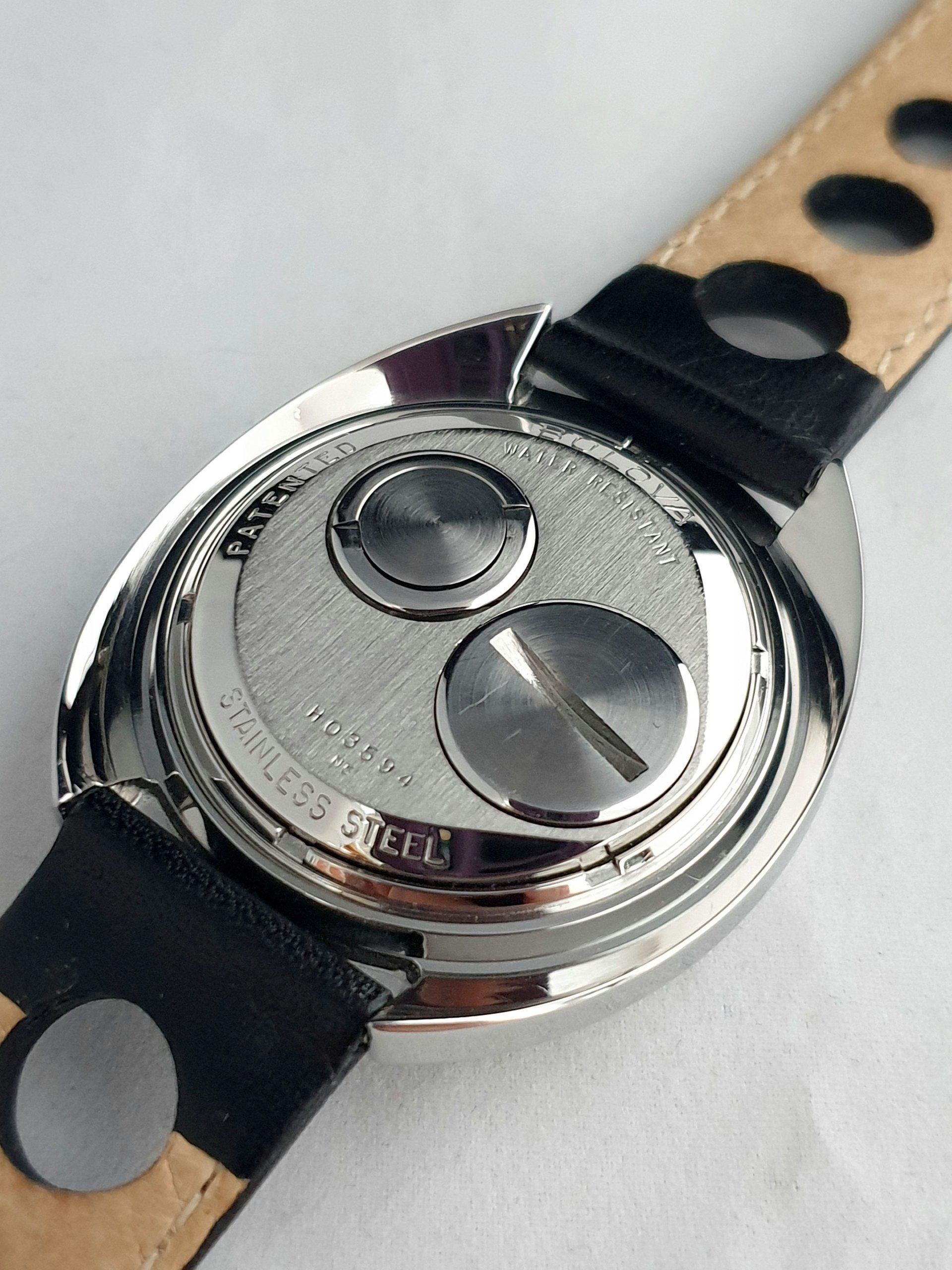 Rear of a silver wristwatch with black leather strap and two polished circular case backs
