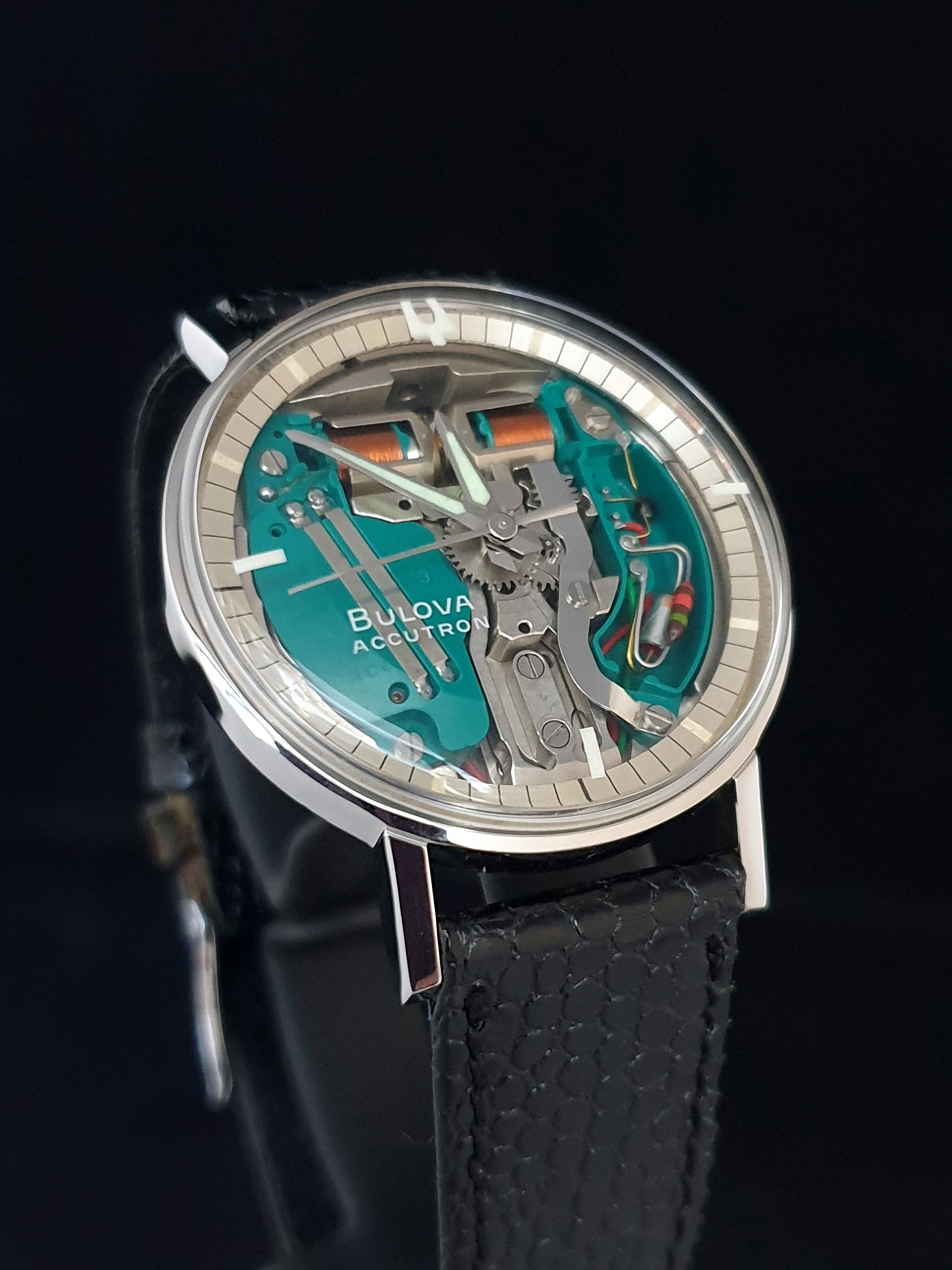 Close-up of a silver mechanical wristwatch with turquoise dial and black strap
