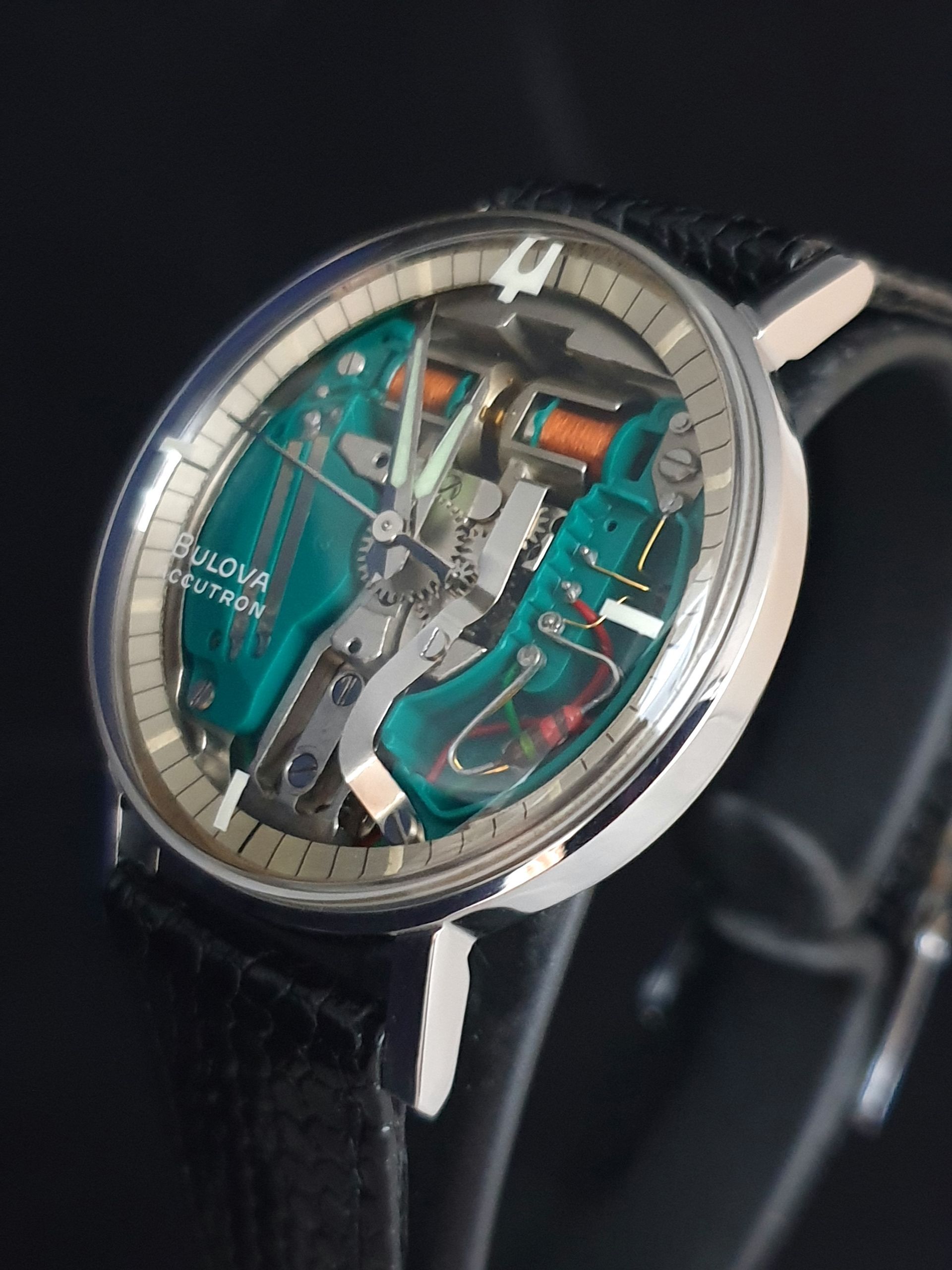 Close-up of a silver wristwatch with a teal skeleton dial and black leather strap