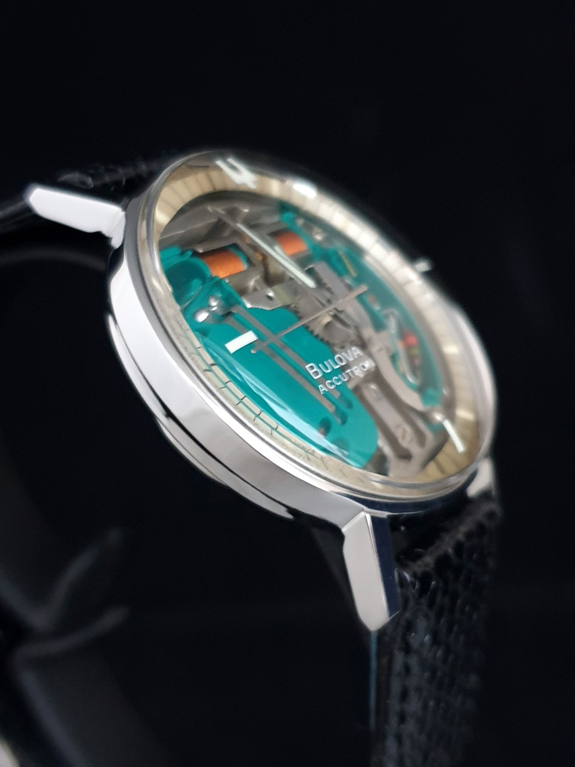 Close-up of a silver wristwatch with a turquoise dial and black strap on a dark background