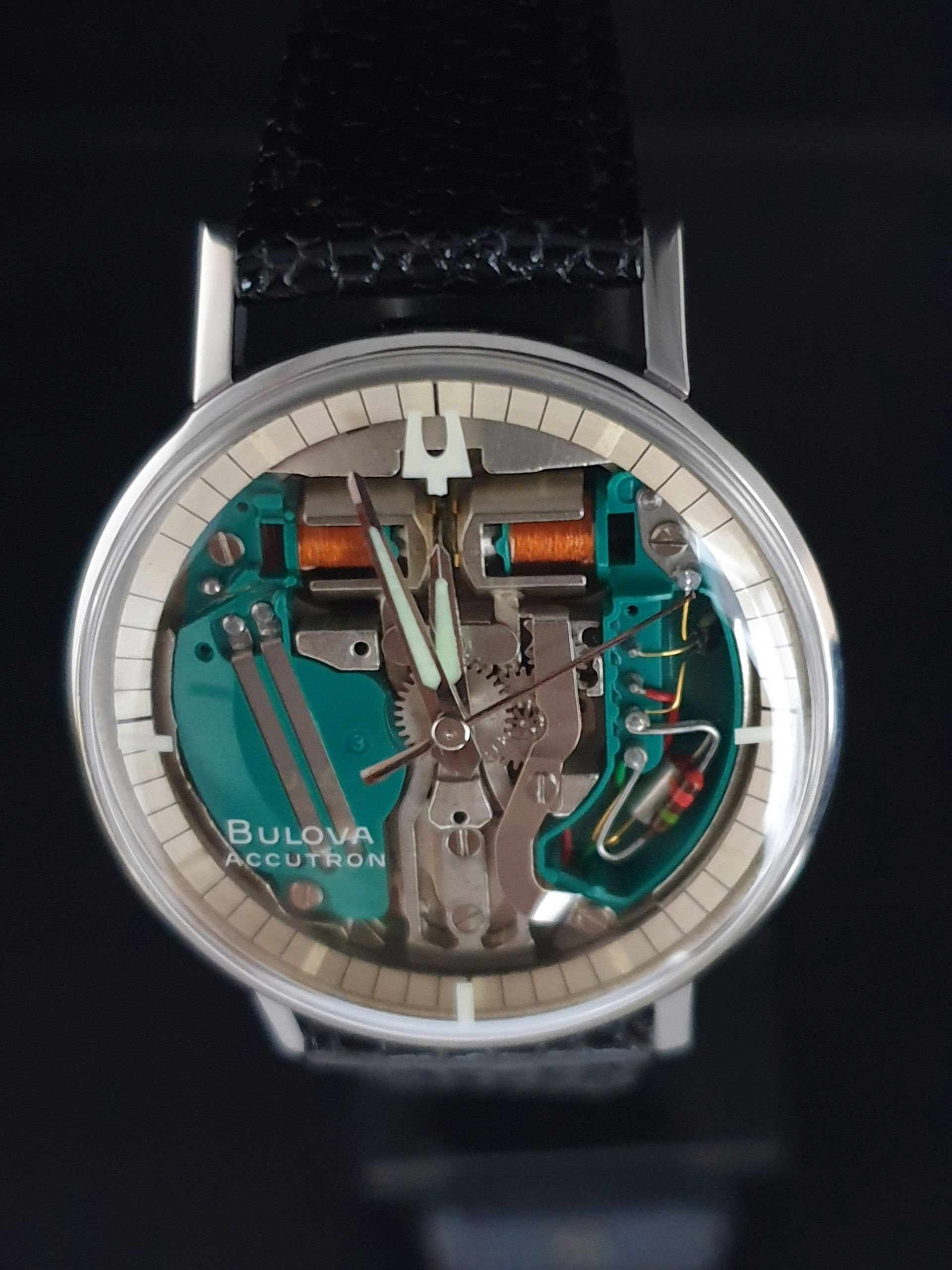 Close-up of a transparent Bulova wristwatch with silver bezel and black strap on a dark background
