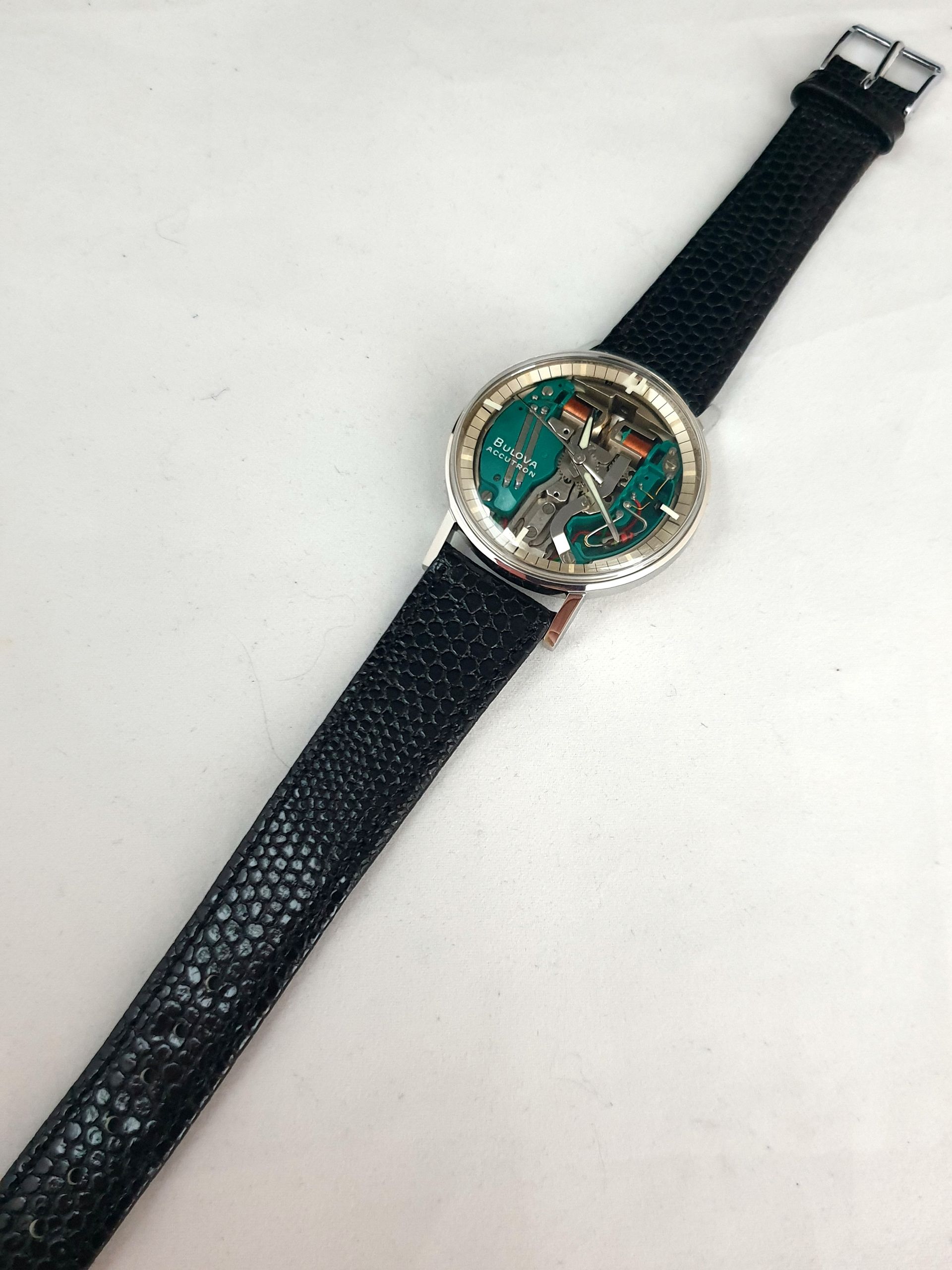Round wristwatch with green dial and black textured strap on a white background