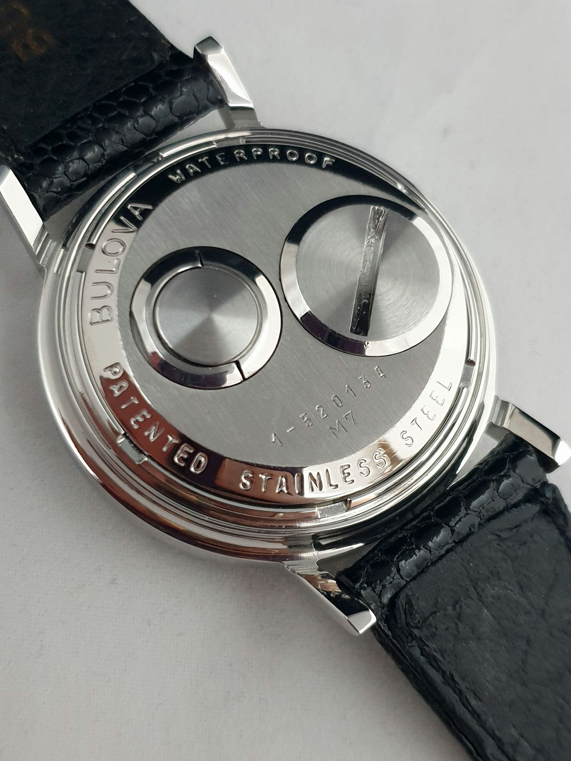 Close-up of a silver wristwatch back with black leather strap and engraved text.