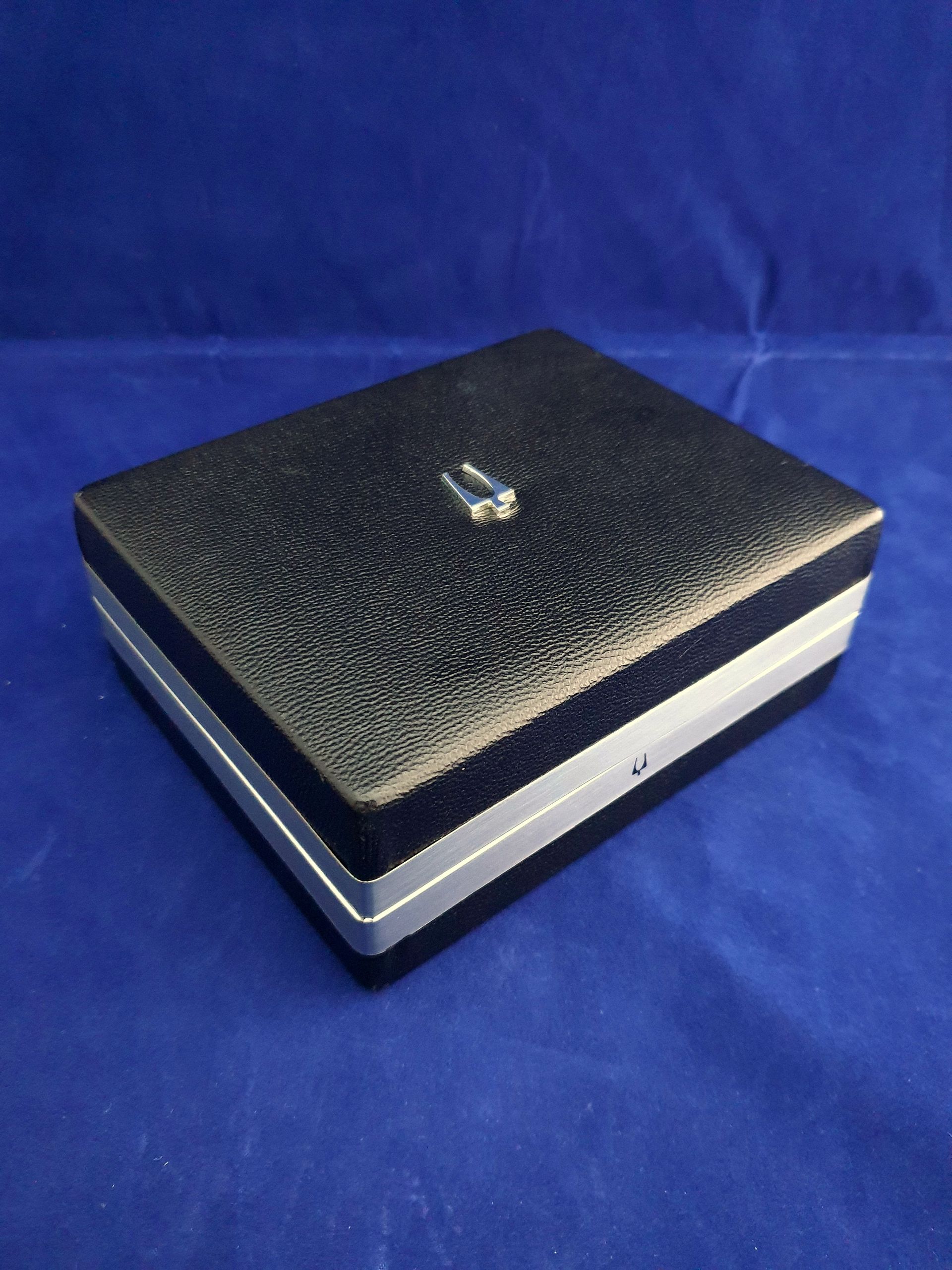 Black textured jewelry box with silver trim on a blue cloth background