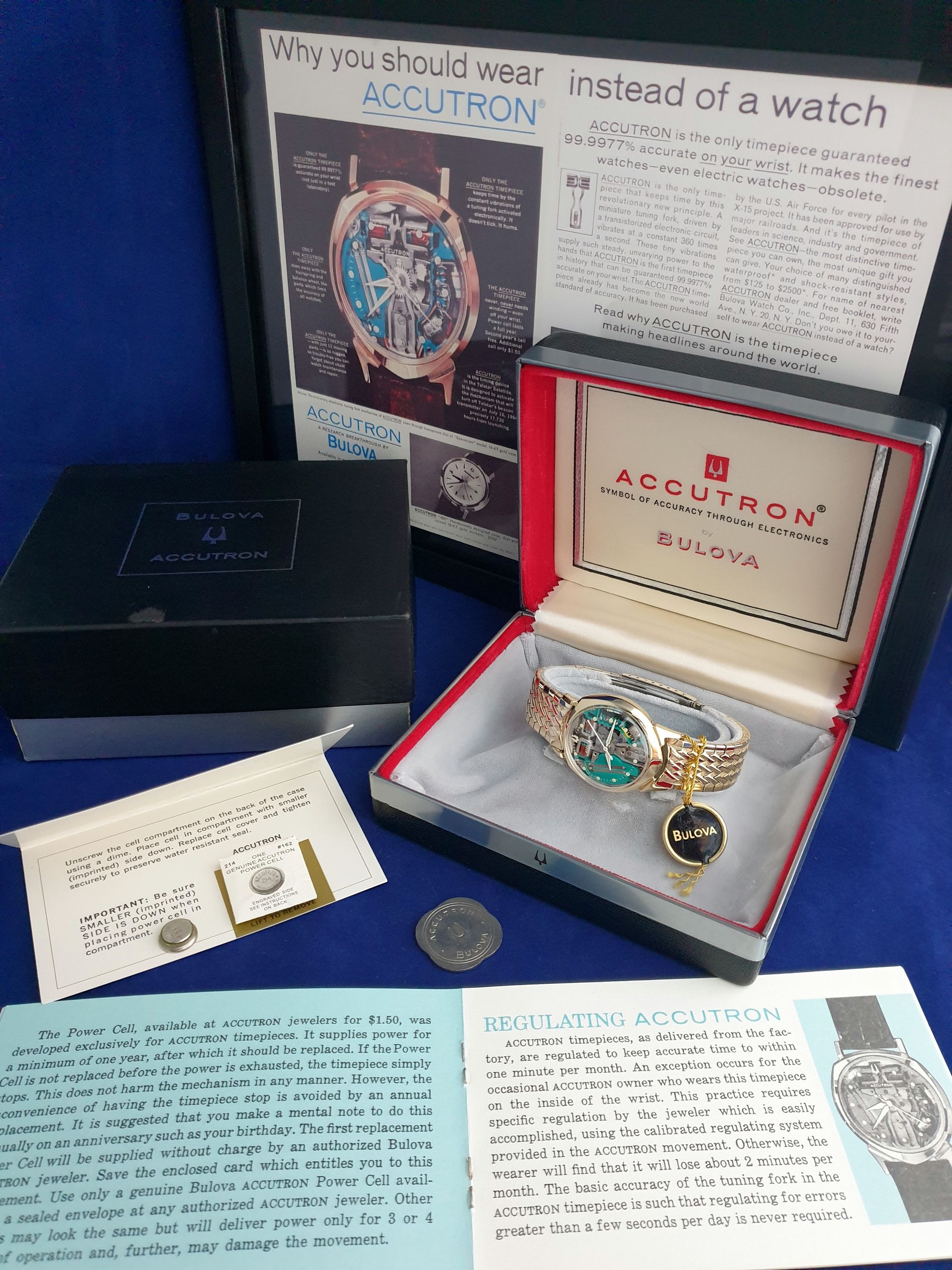 Accutron watch display with open case, brochures, and vintage advertising posters on a blue wall.