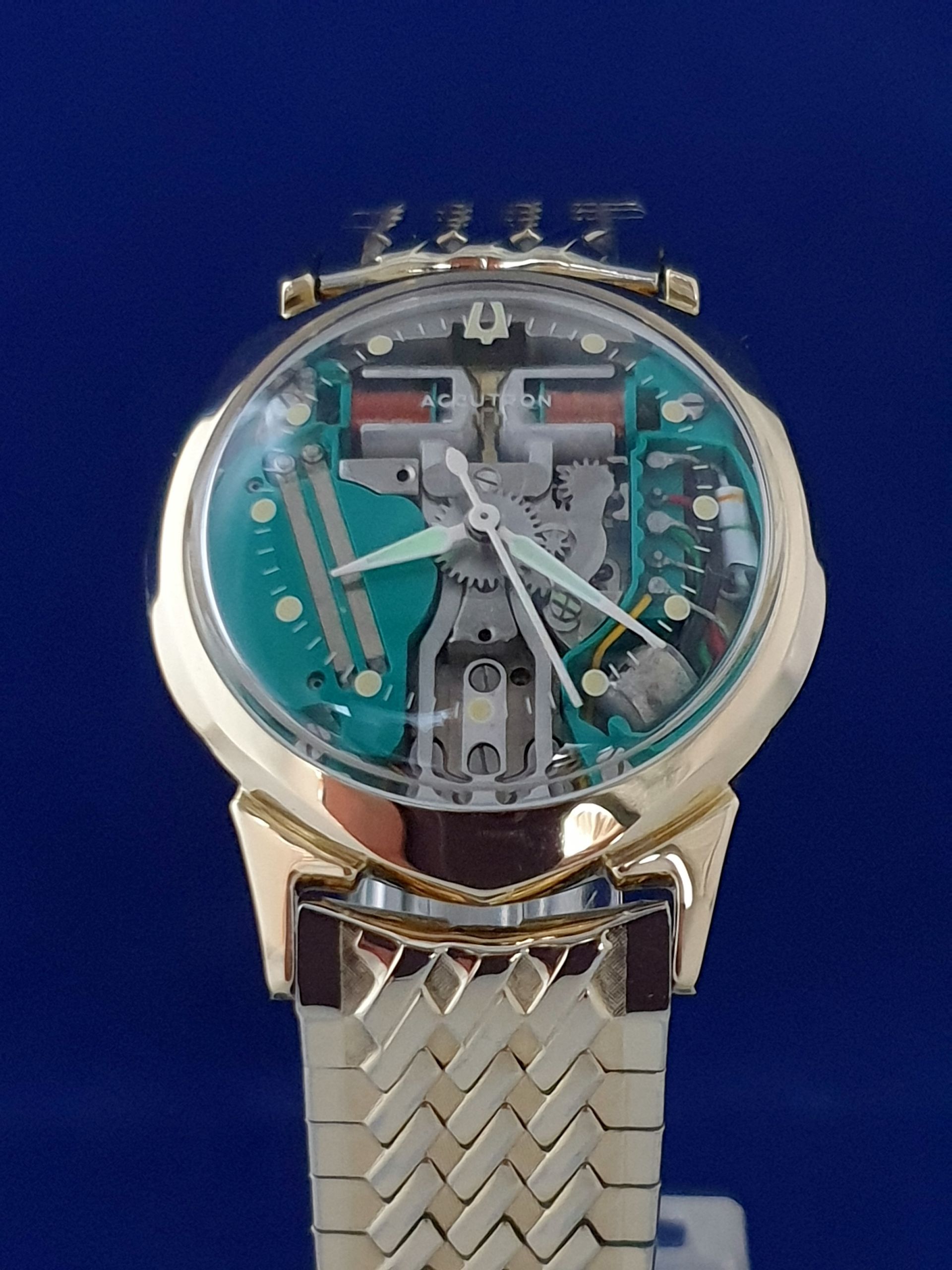 Gold wristwatch with a transparent skeleton dial and silver metal band on a blue background