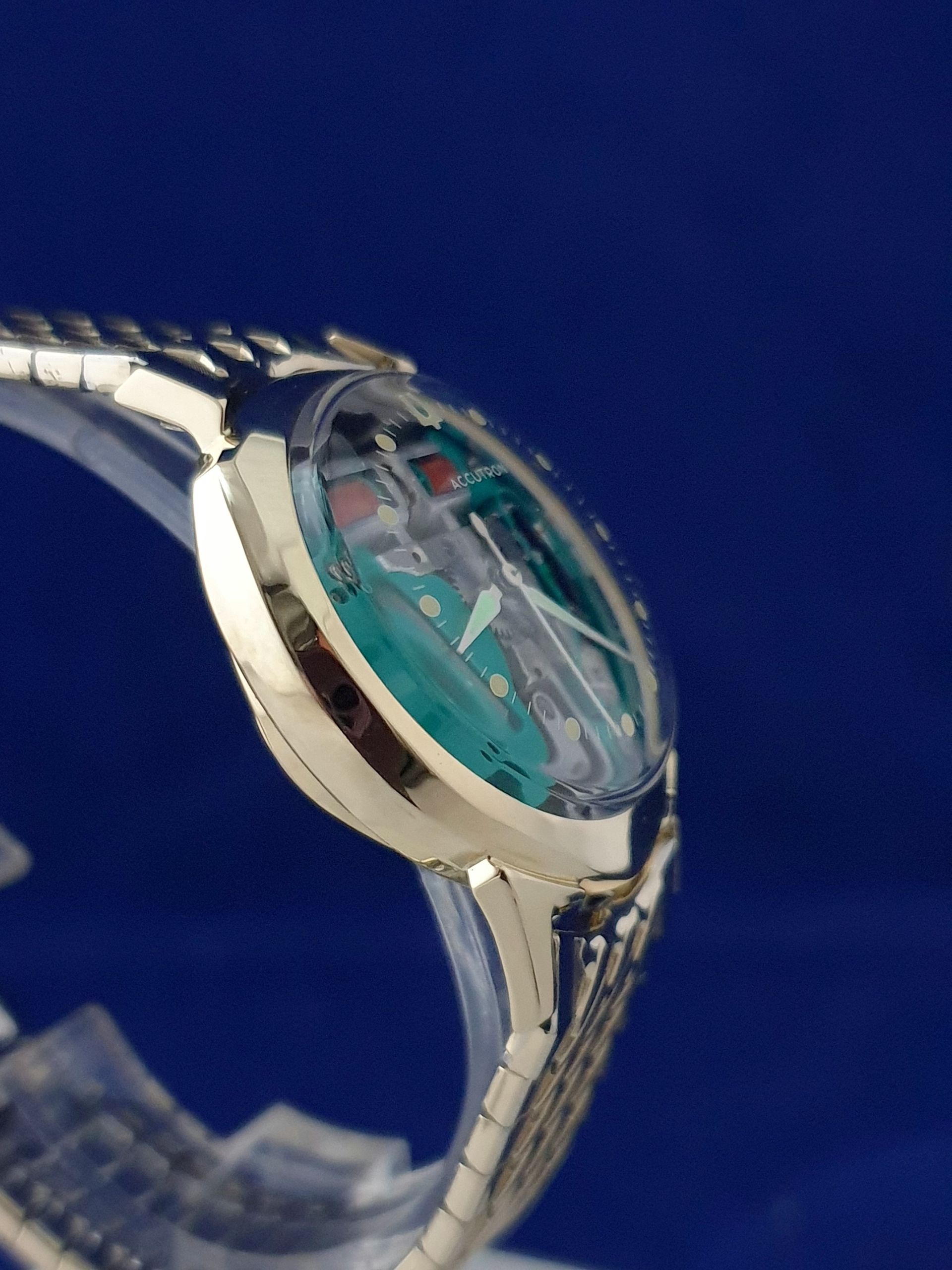 Silver wristwatch with a turquoise face and metal band against a blue background