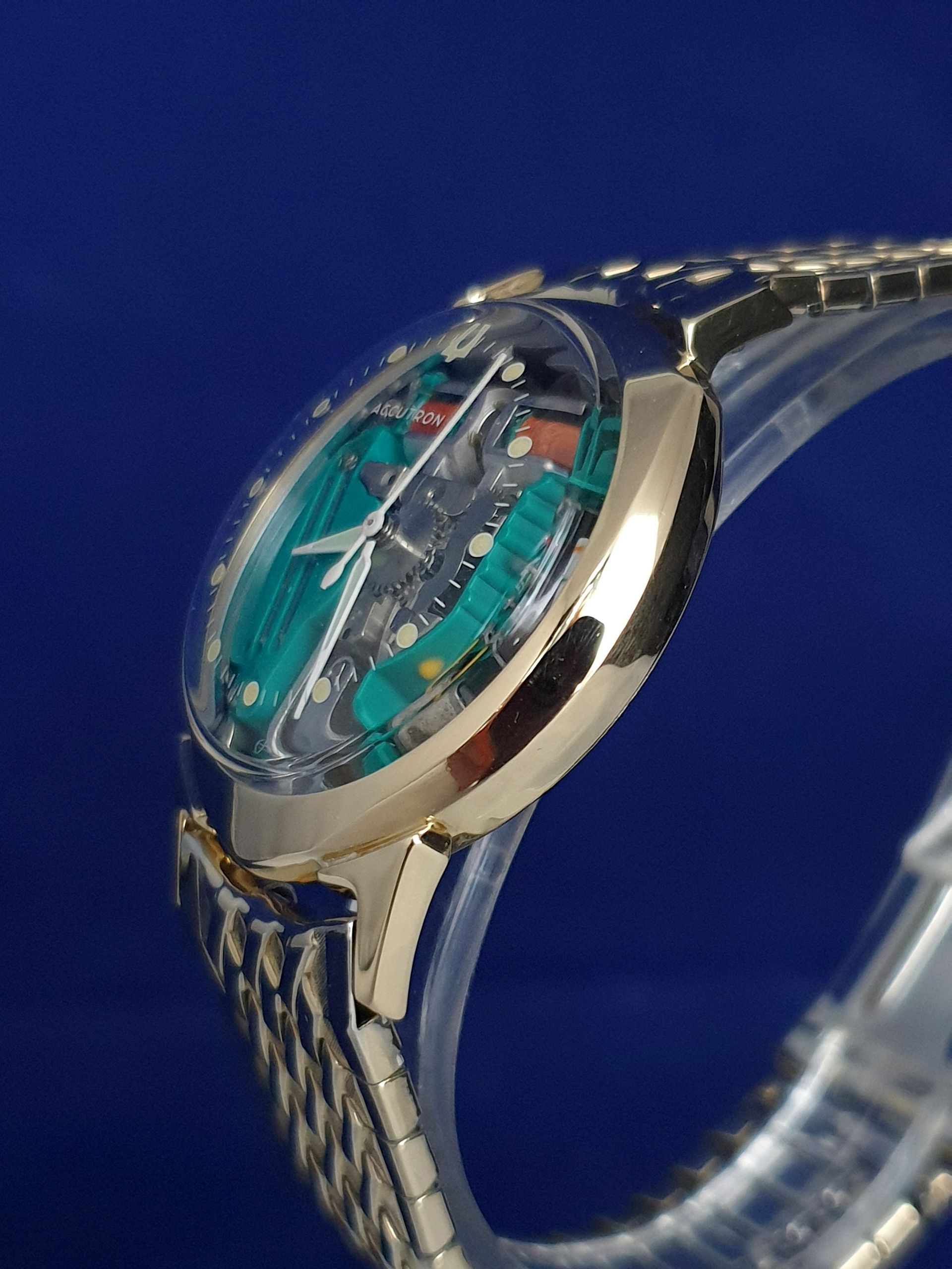 Close-up of a silver wristwatch with a transparent turquoise face on a blue background