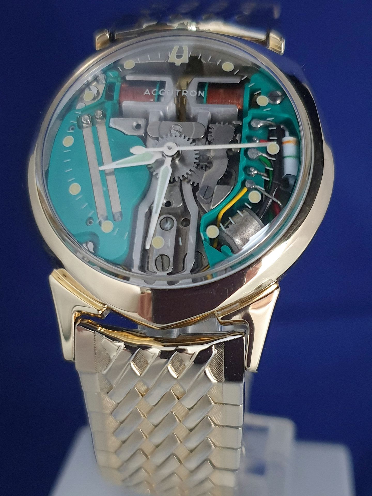 Skeleton wristwatch with turquoise dial and silver metal bracelet on a blue background