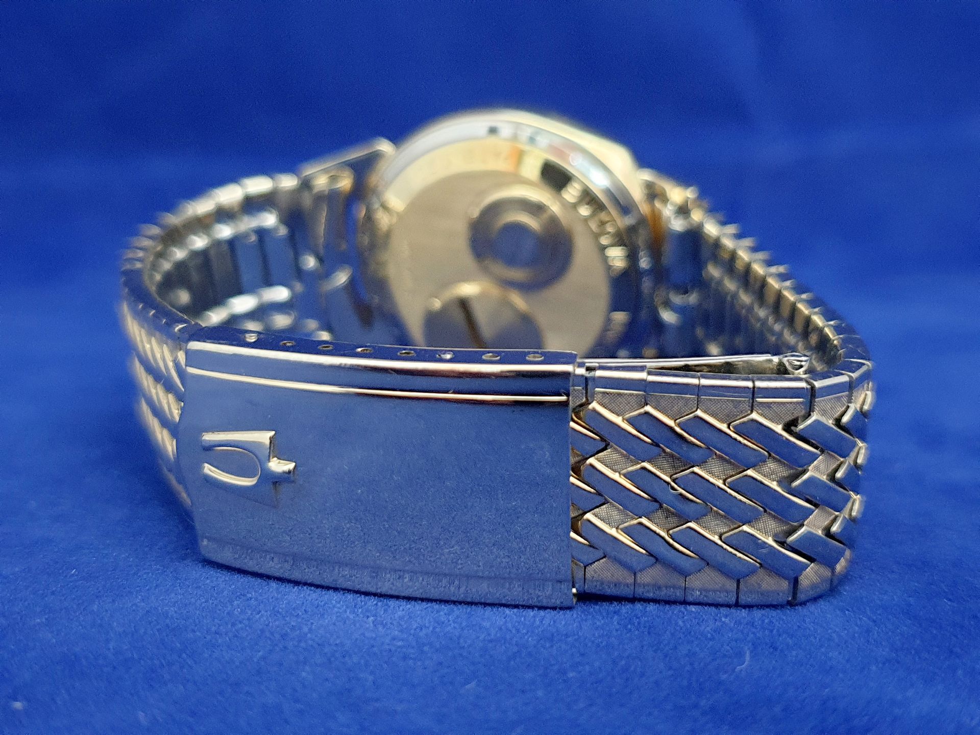 Silver metal wristwatch with linked band and clasp, viewed from the back on a blue background