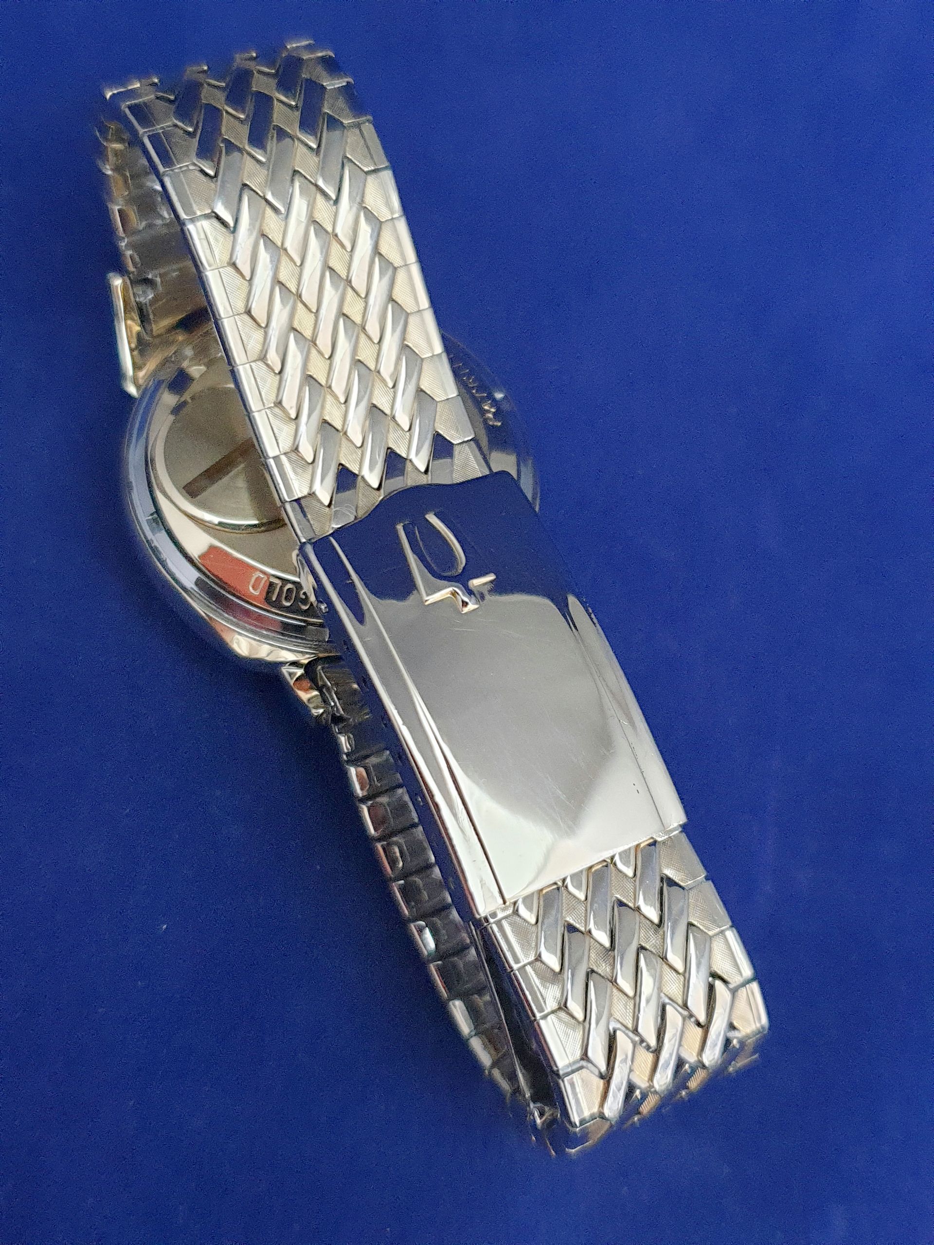 Silver metal wristwatch band with a folded clasp on a blue background