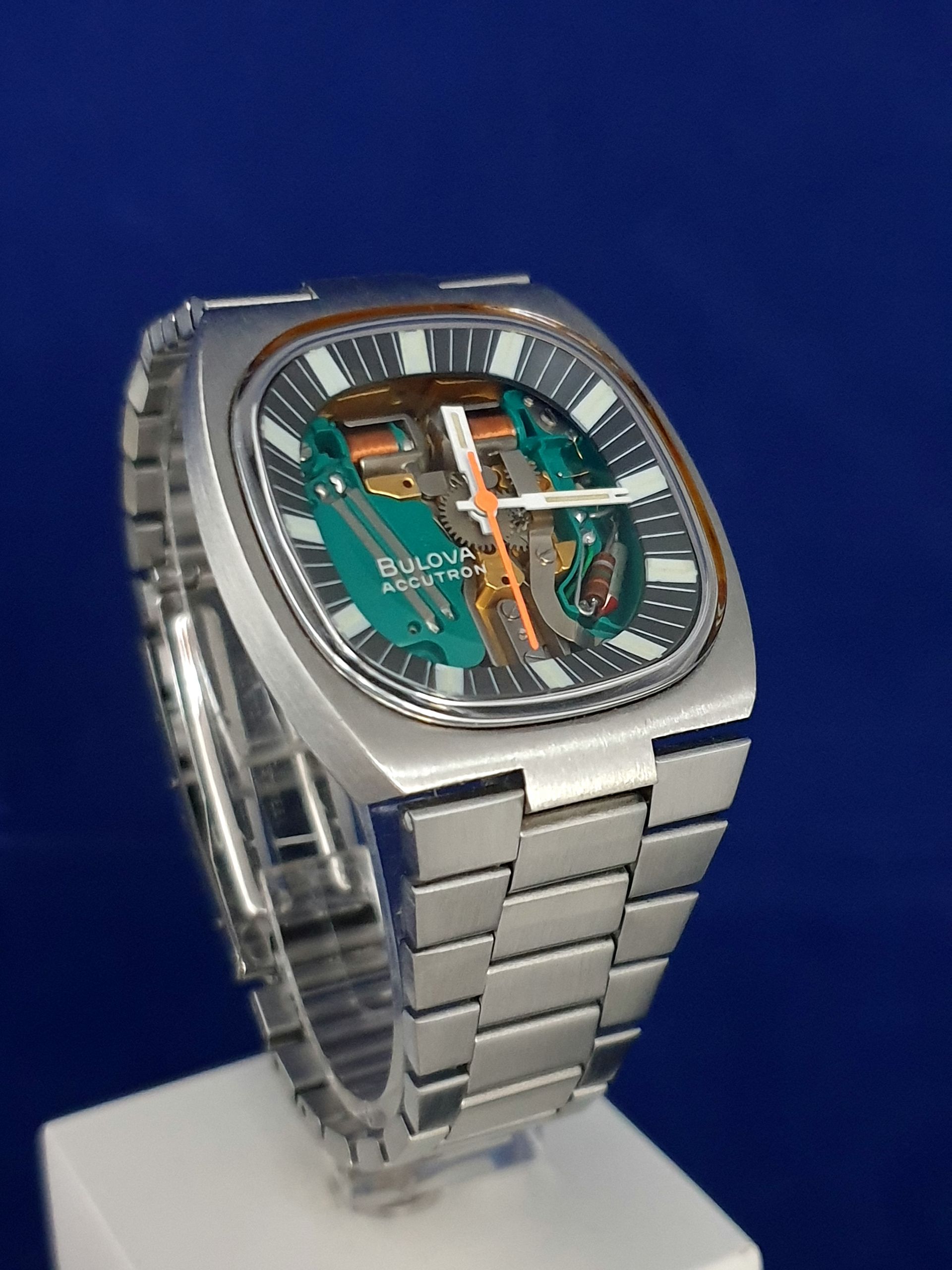 Silver watch with a striped dial and orange accents on a white display stand against a blue background