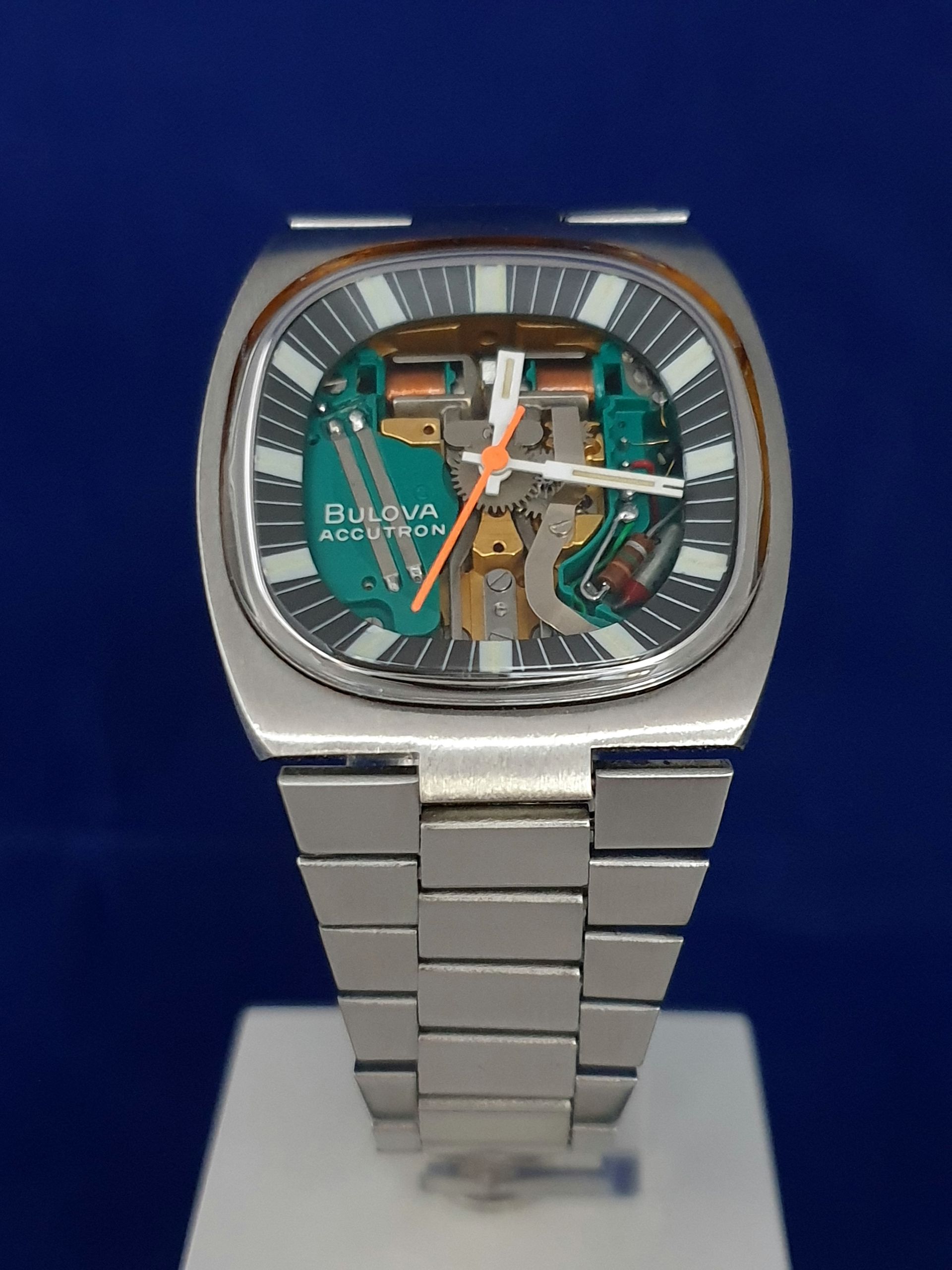 Silver square wristwatch with turquoise skeleton dial on a blue background