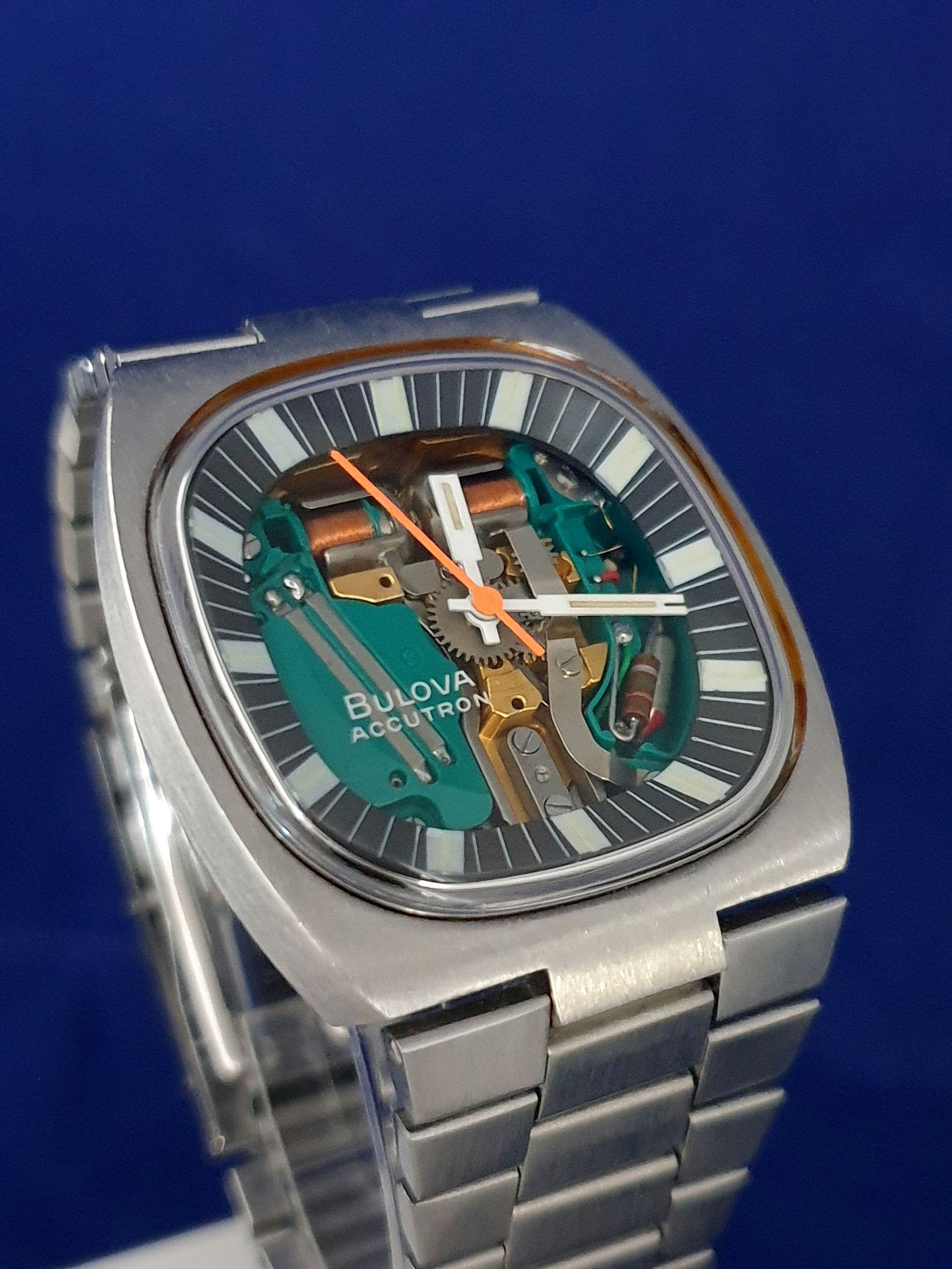 Close-up of a silver luxury wristwatch with a skeleton dial and metal bracelet on a blue background