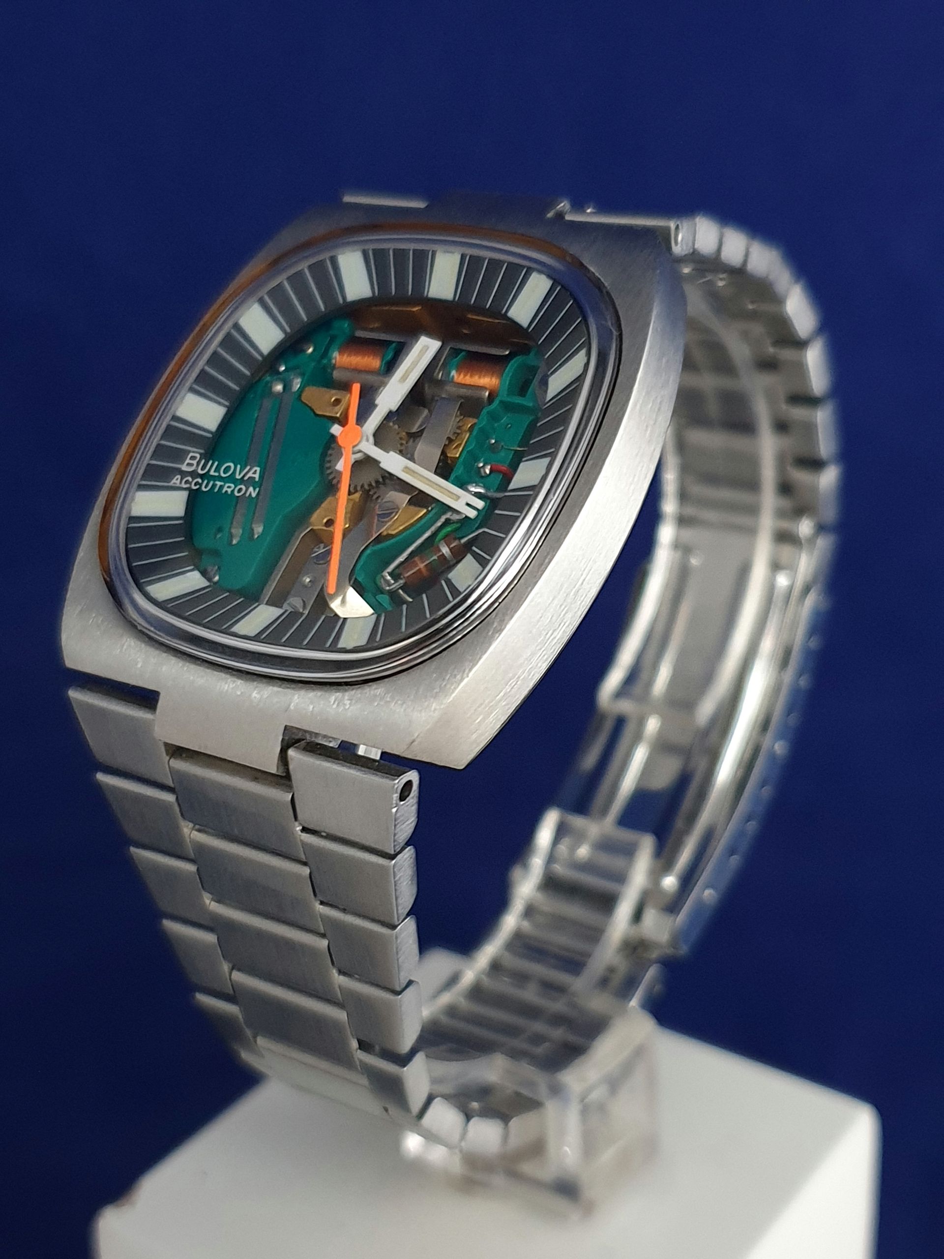 Silver wristwatch with teal dial and orange accents on a display stand