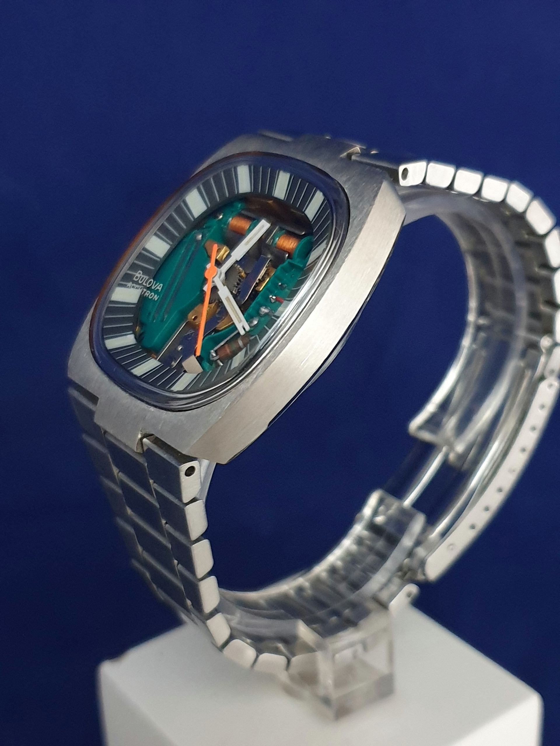 Silver wristwatch with a teal dial on a display stand against a dark blue background