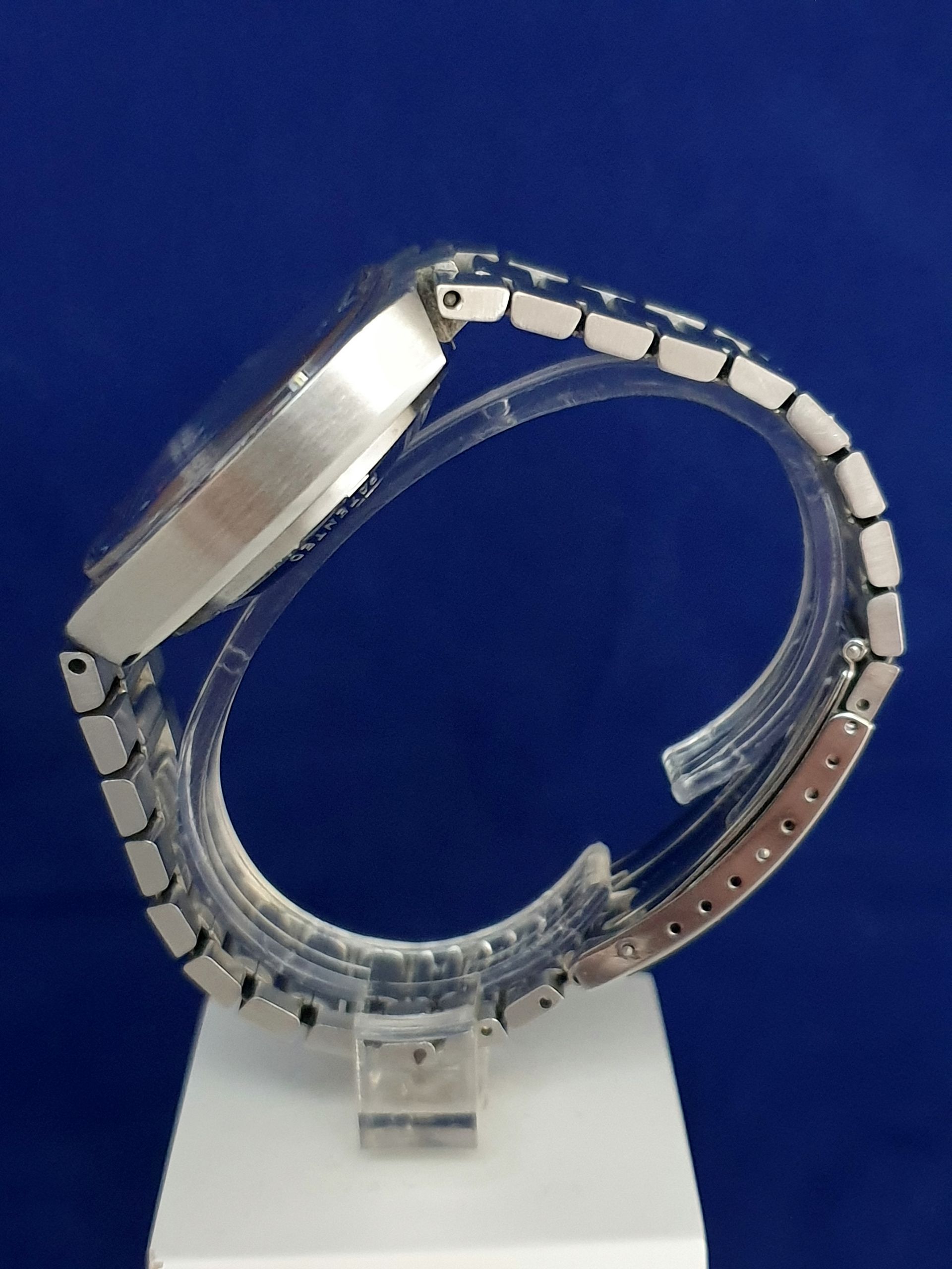 Modern silver wristwatch with a clear band displayed on a white stand against a blue background