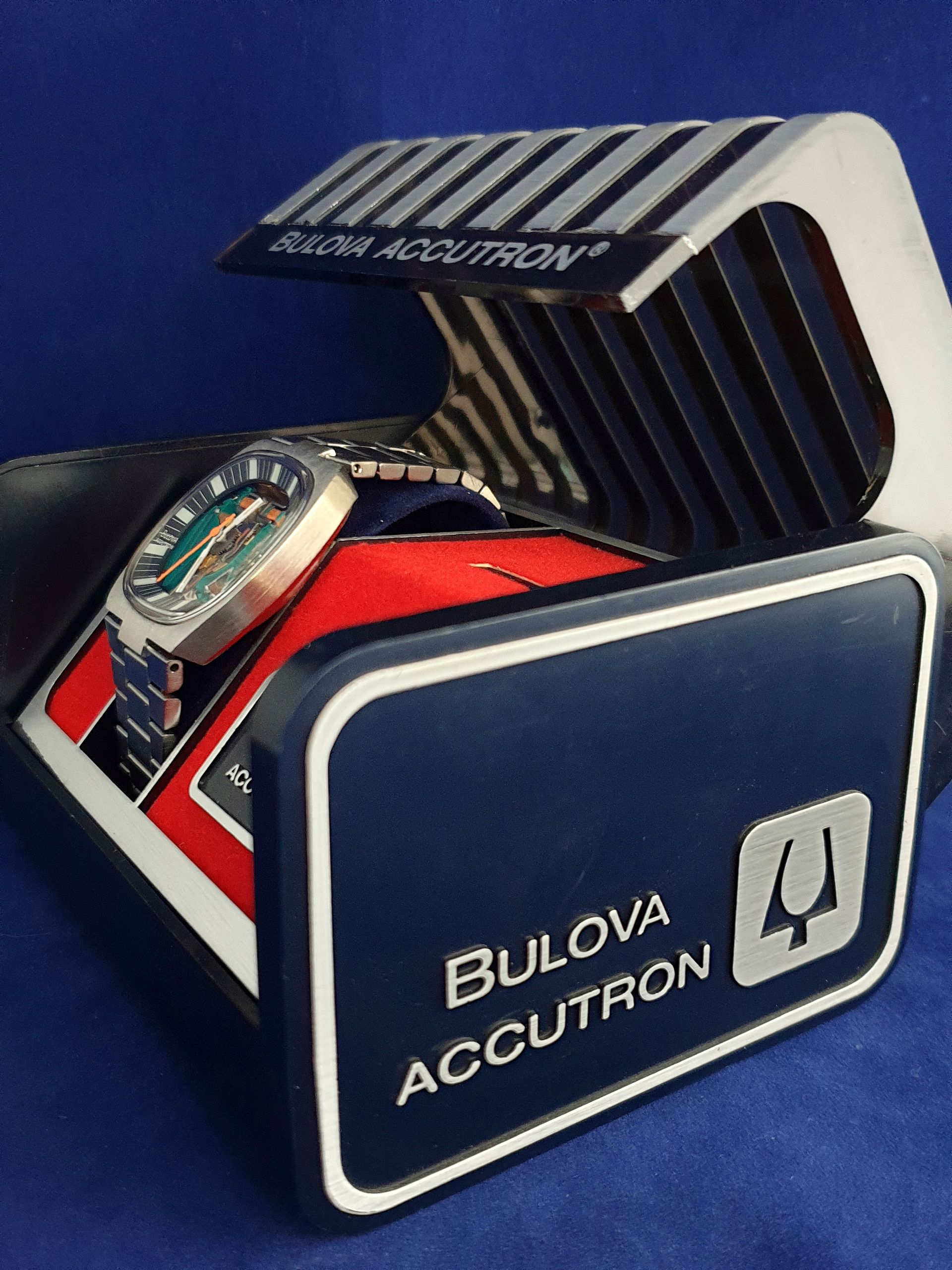 Bulova Accutron watch display on a blue background, featuring a retro striped cover and clock face