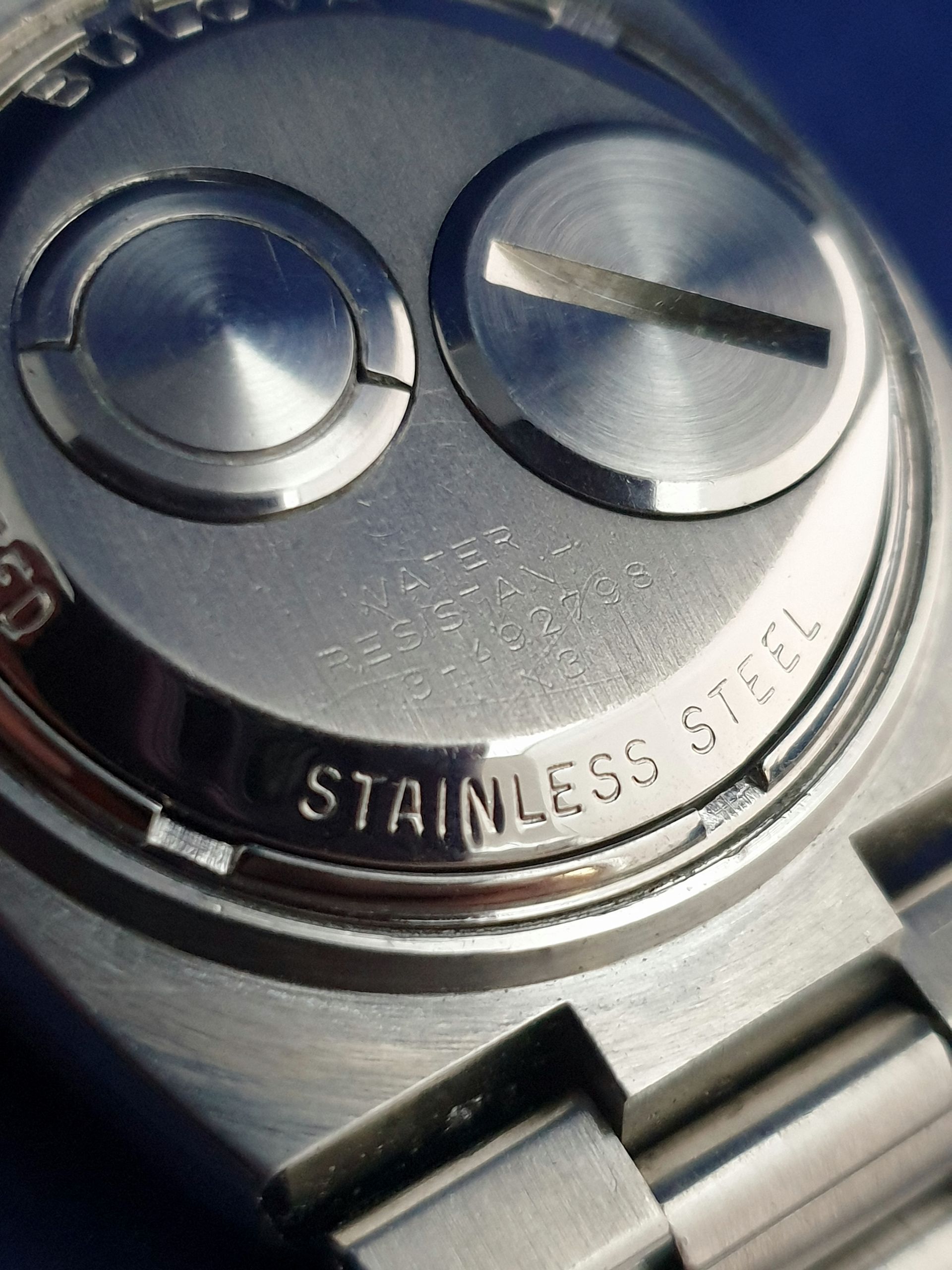 Close-up of a stainless steel watch case back with two screws and brushed metal finish