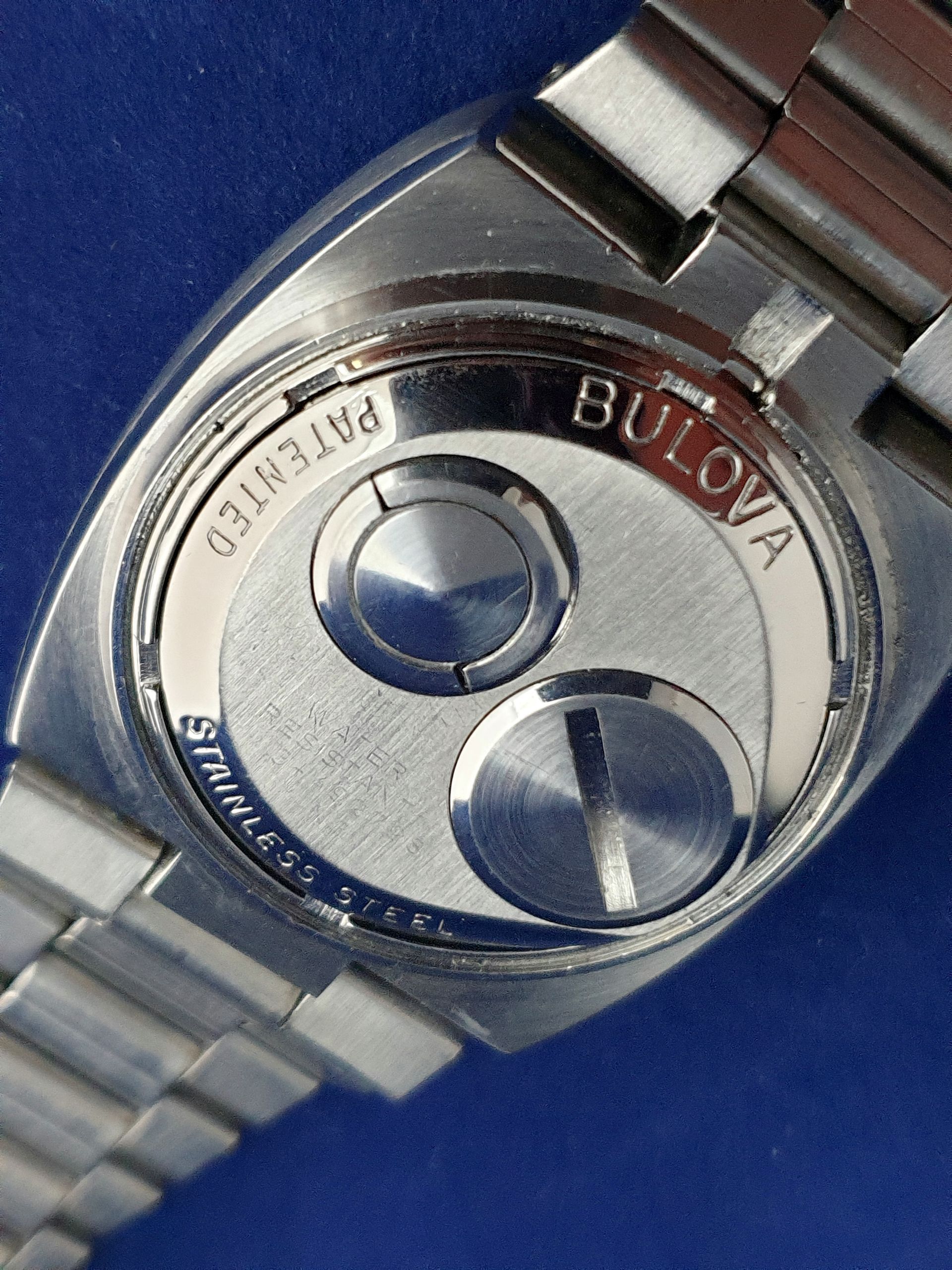 Close-up of a Bulova watch back with a silver metal bracelet on a blue background