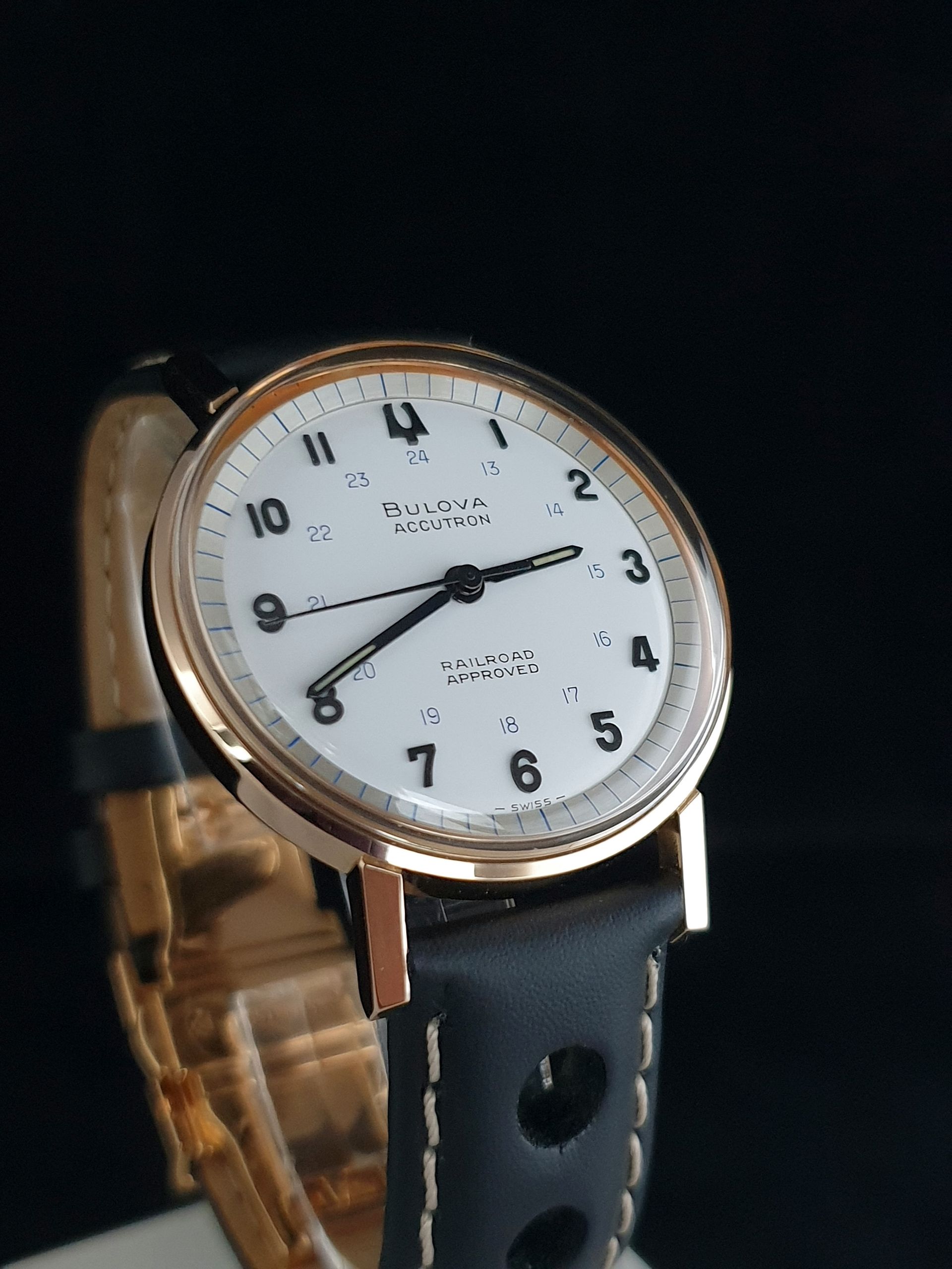 Rose gold wristwatch with white dial and black leather strap on a dark background