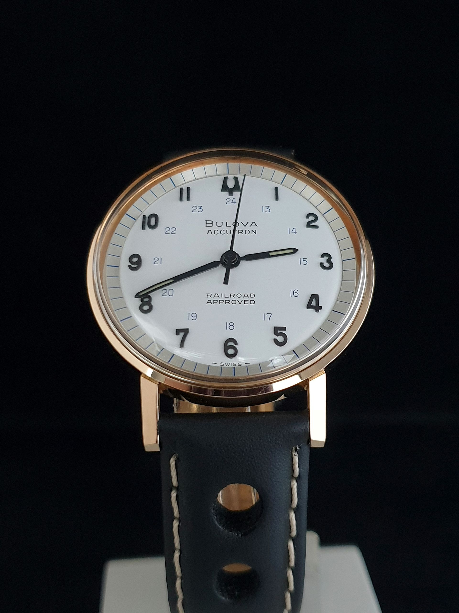 Gold-and-black wristwatch with white dial and black leather strap on a dark background