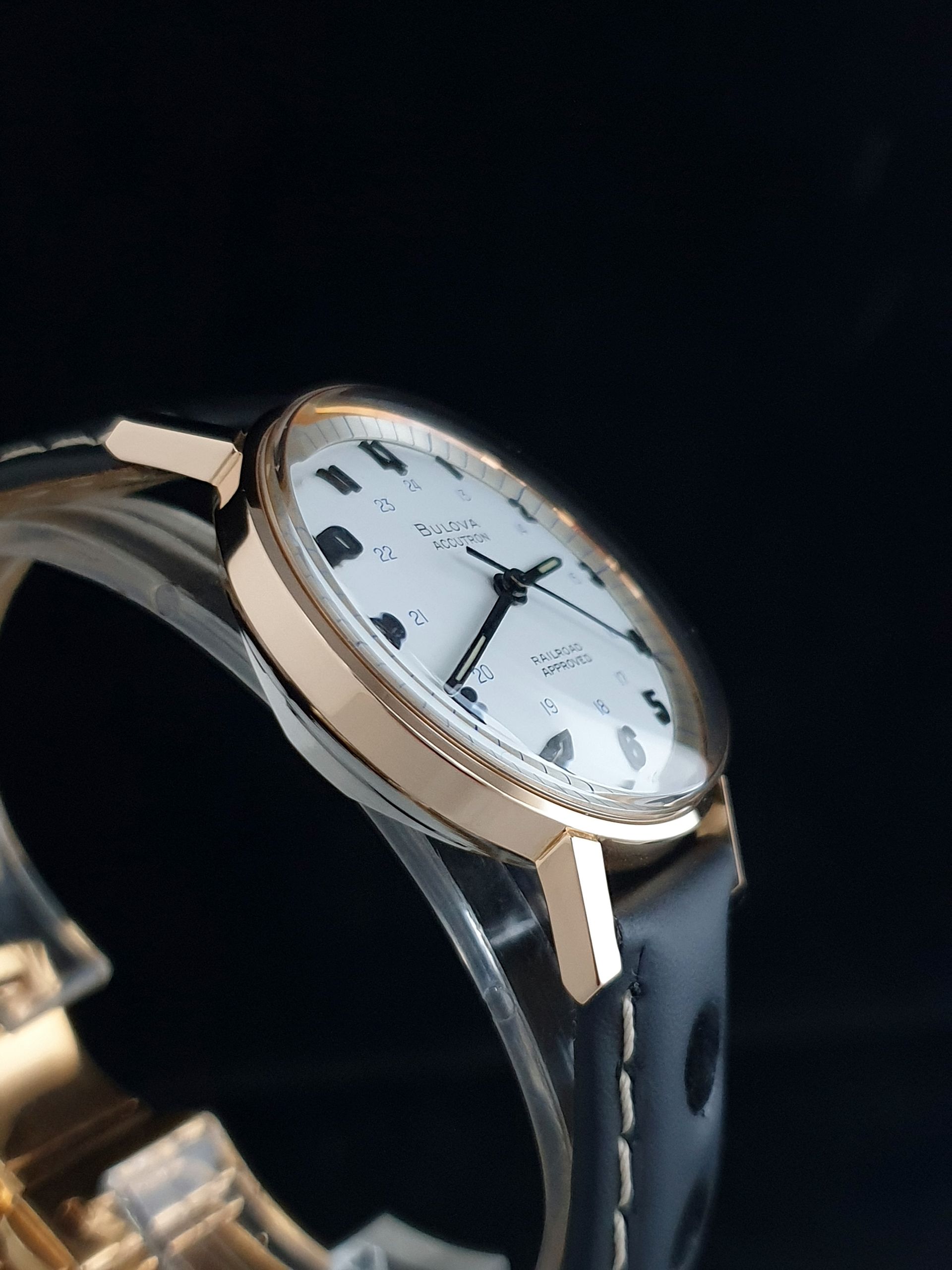 Close-up of a gold wristwatch with a white dial and black leather strap on a dark background