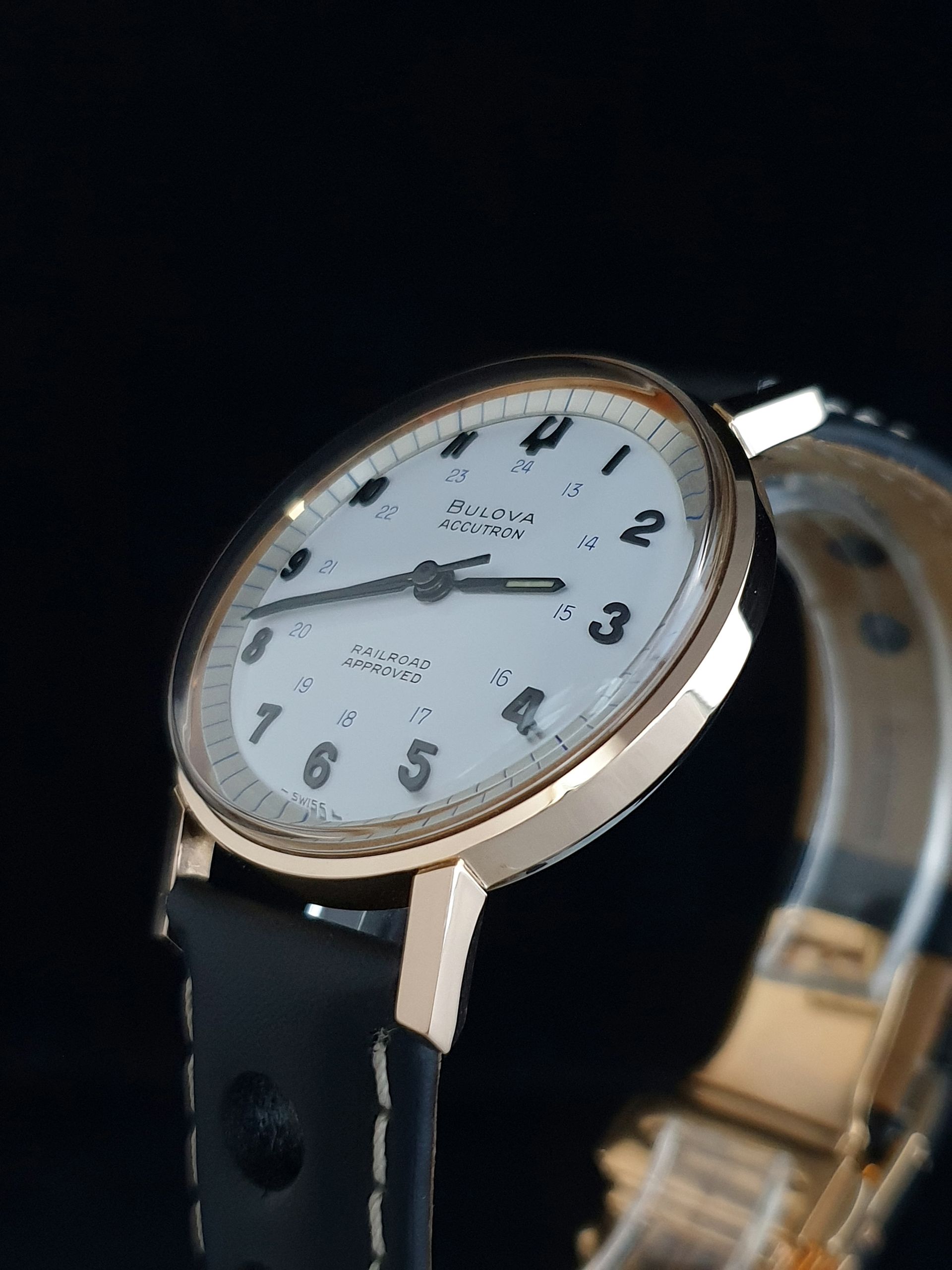 Close-up of a rose gold wristwatch with a white dial and black leather strap on a dark background