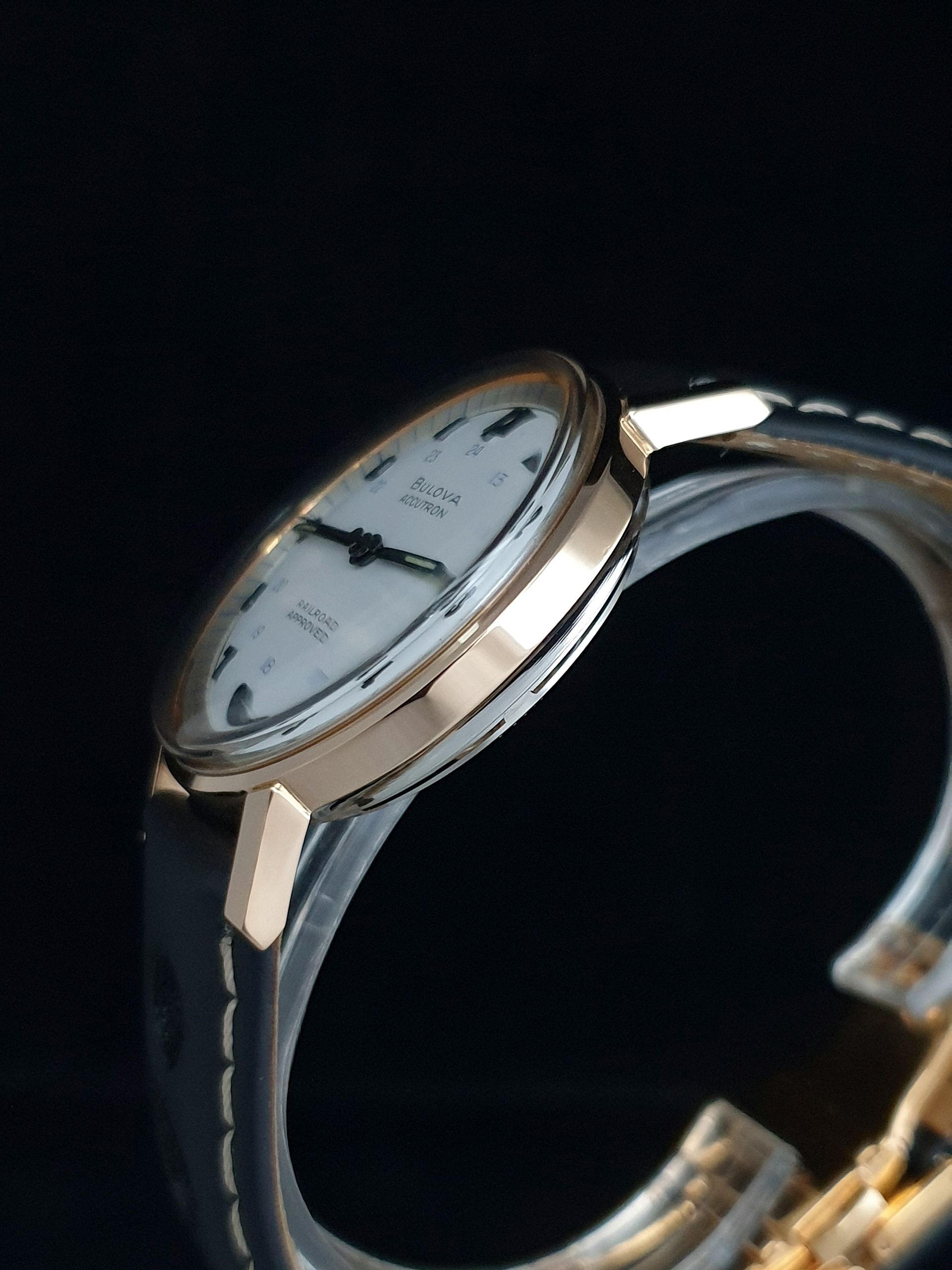 Silver wristwatch with a white dial and black leather strap on a dark background