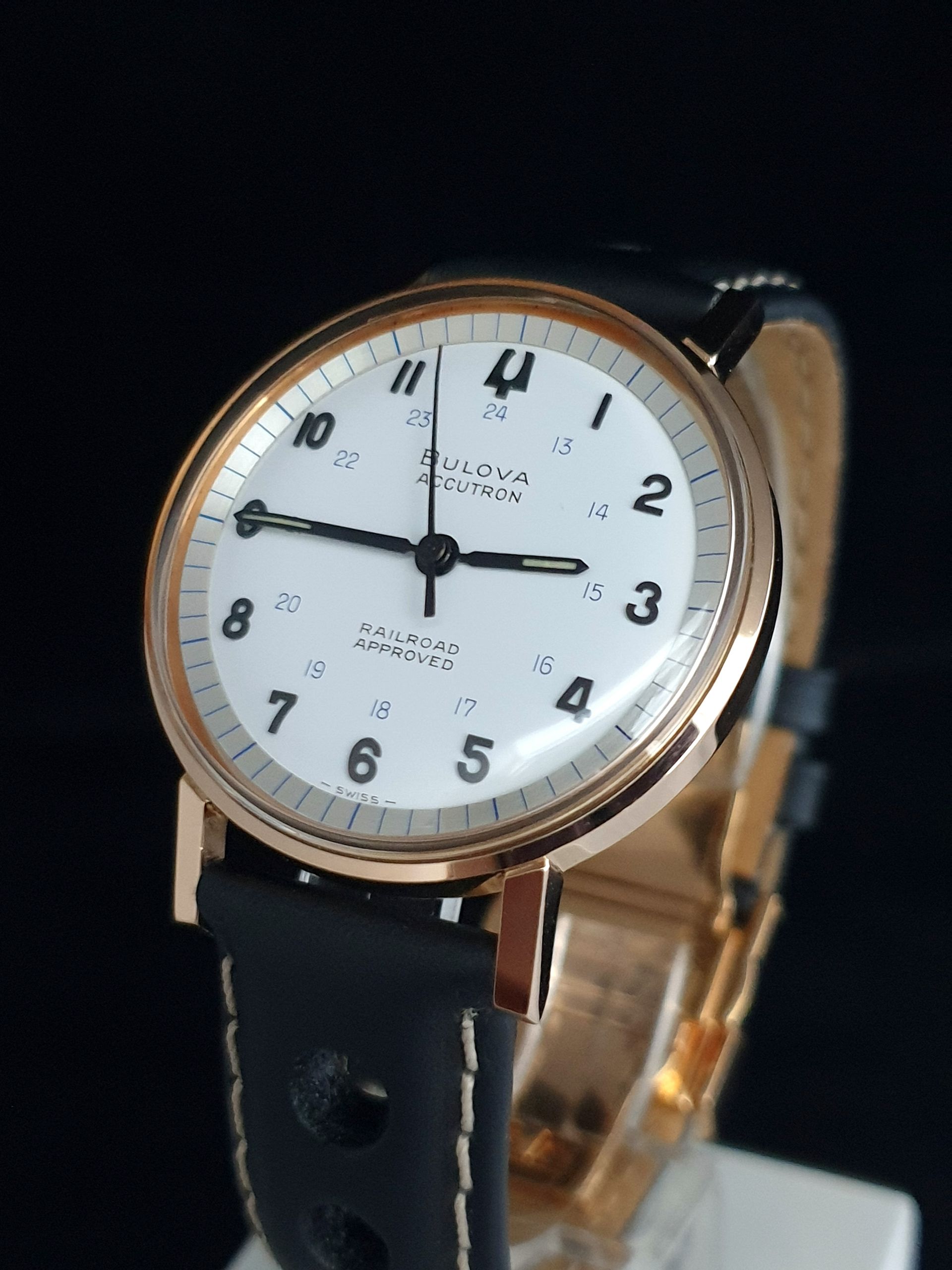 Close-up of a rose gold wristwatch with a white dial and black leather strap on a dark background