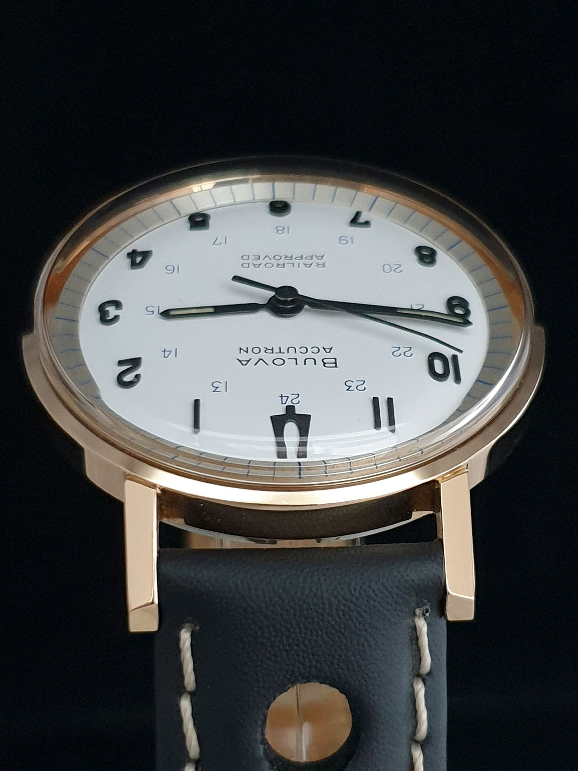 Gold watch with white face and black leather strap on a dark background