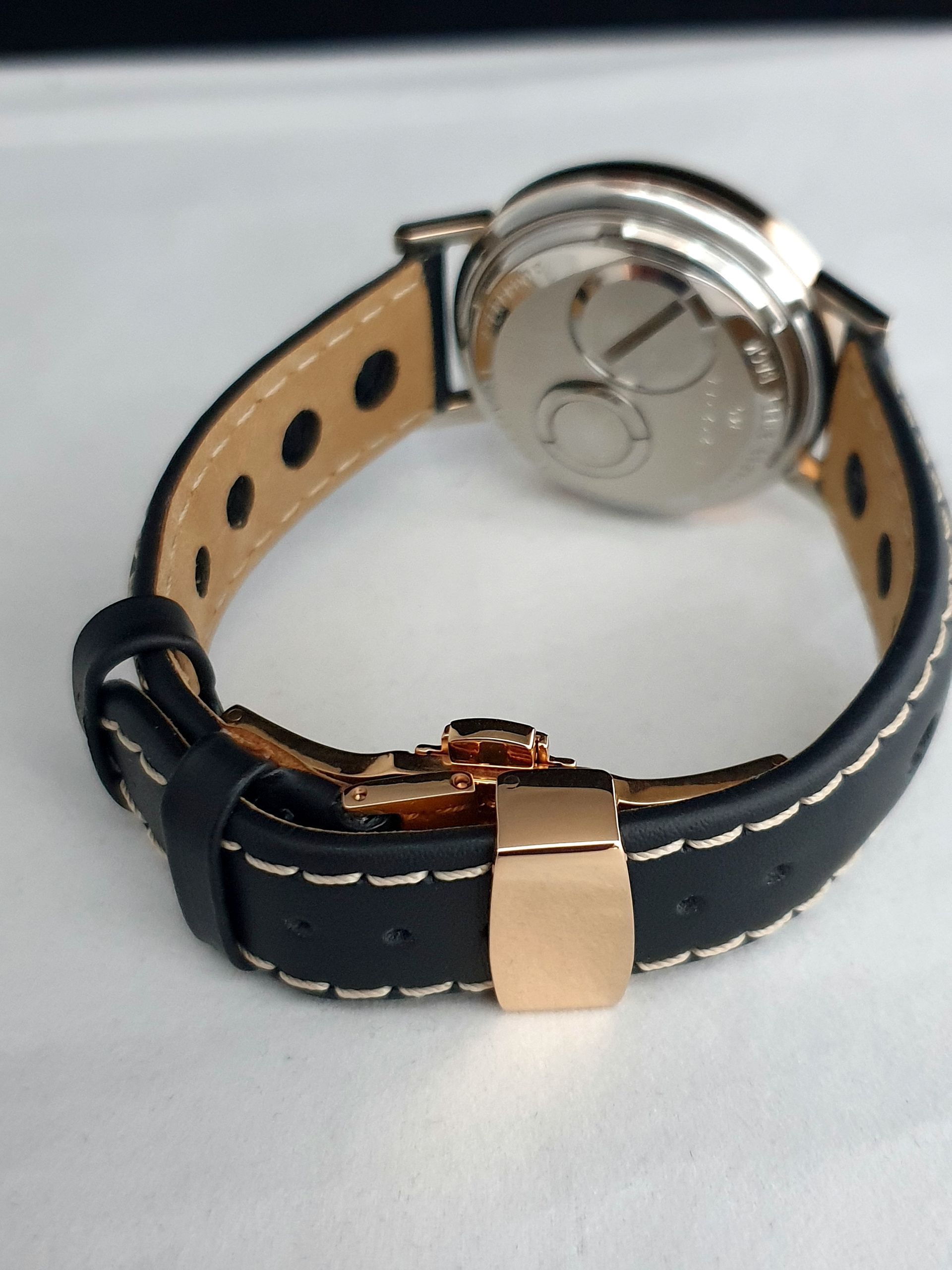 Close-up of a black and tan watch band with a silver clasp on a white surface