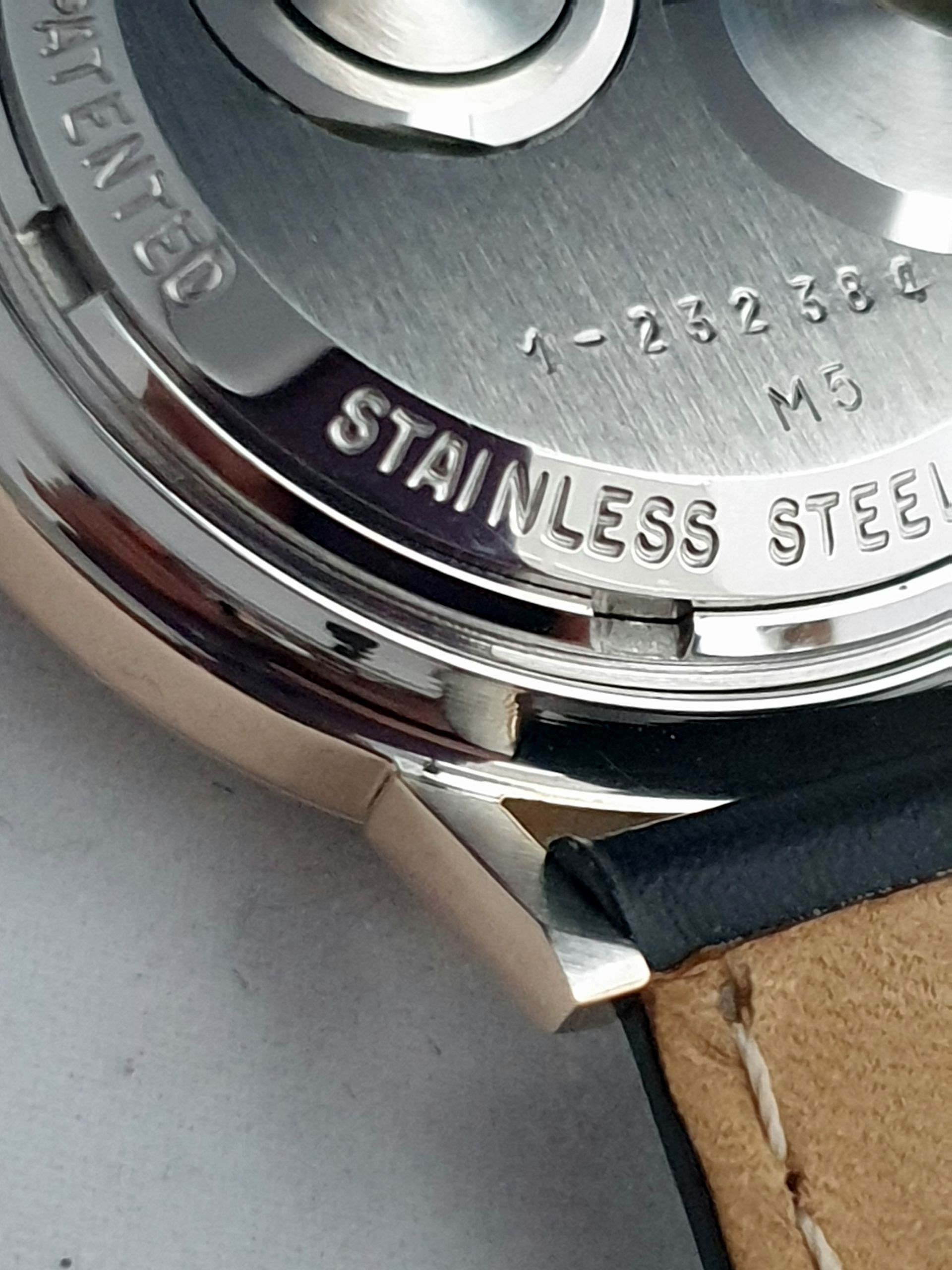 Close-up of a watch case back with engraved stainless steel and a brown leather strap