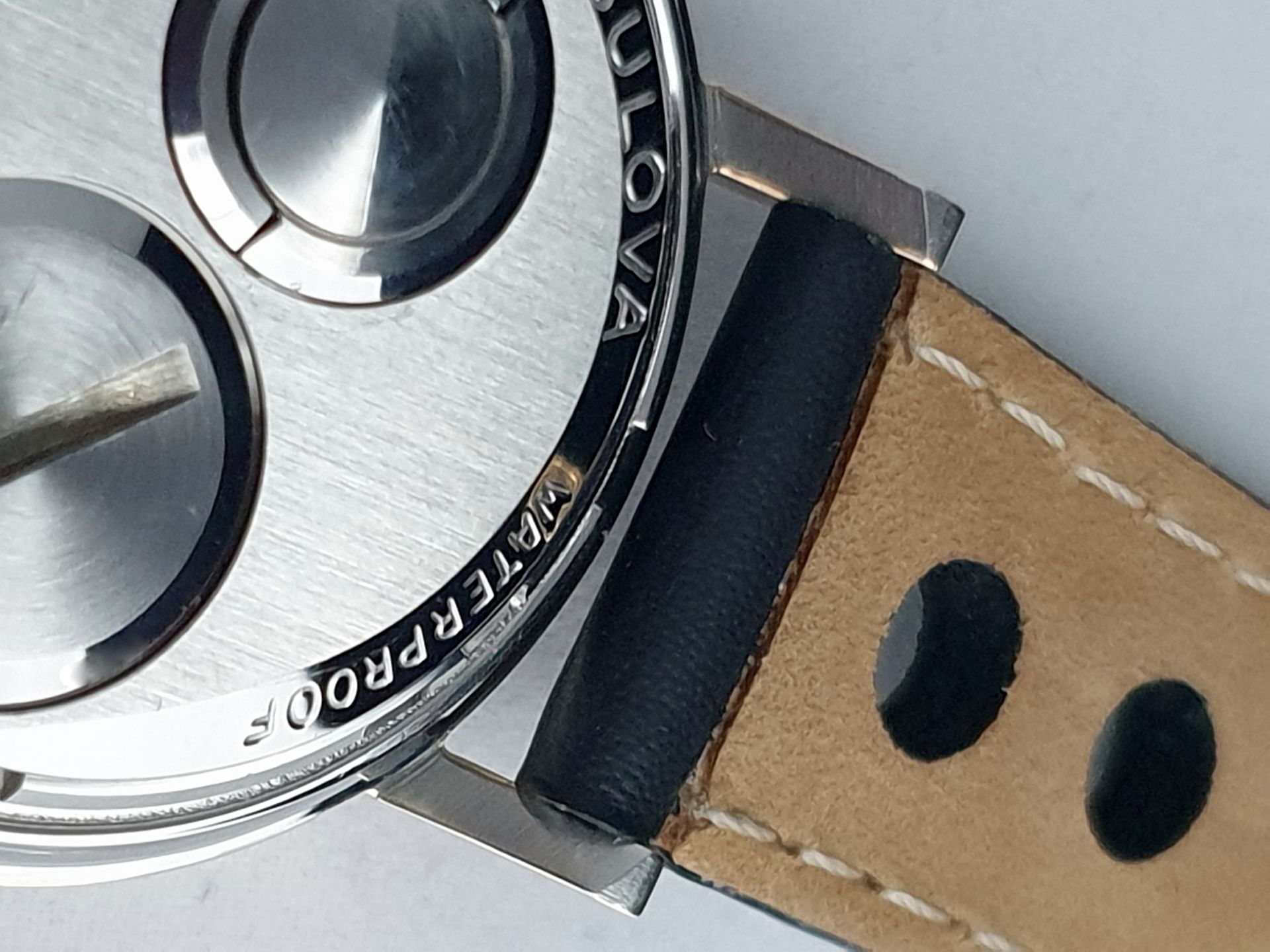 Close-up of a silver watch case attached to a brown leather strap with black stitching