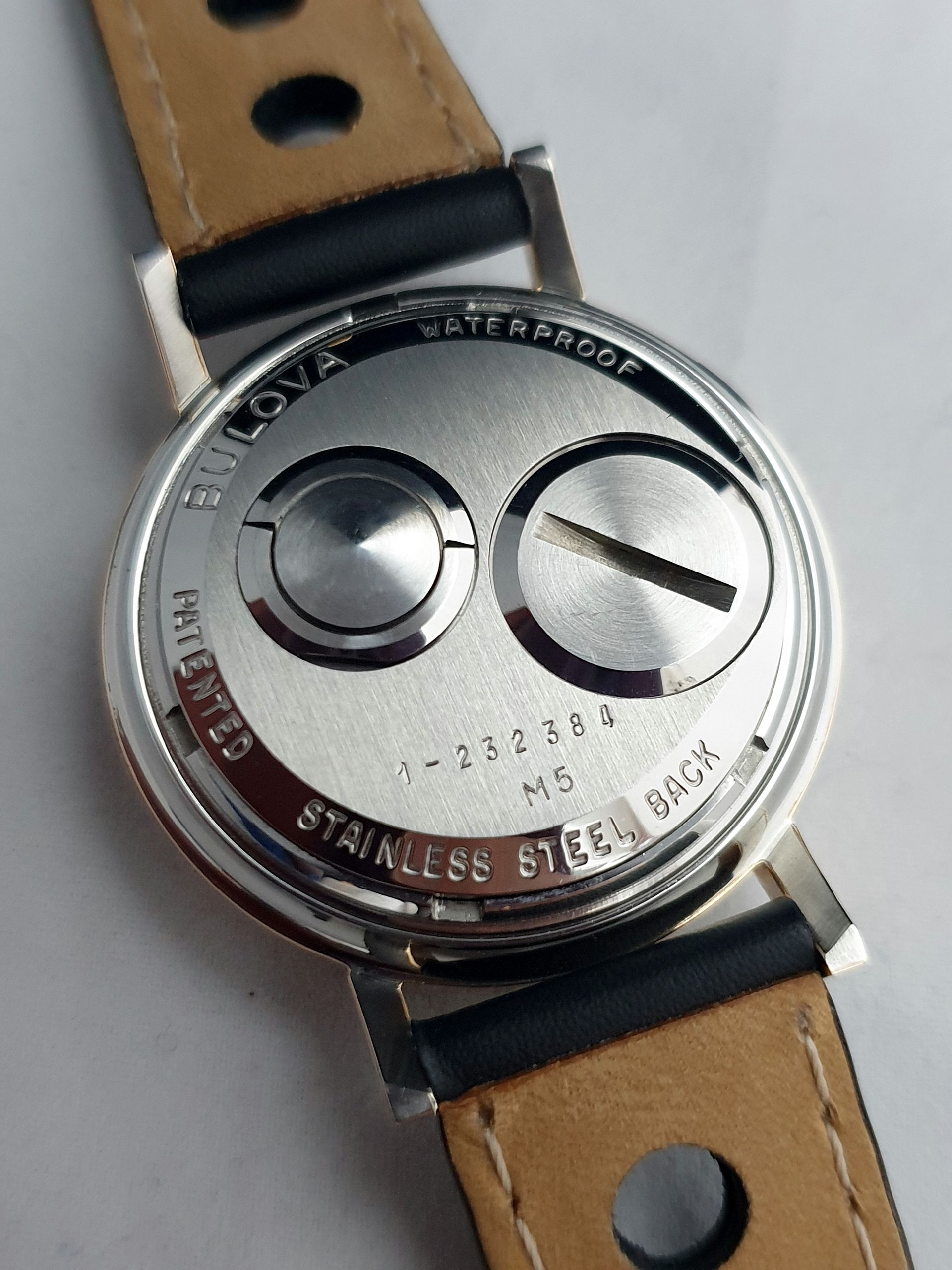 Close-up of a silver watch back with tan leather strap, engraved stainless steel and exposed mechanisms