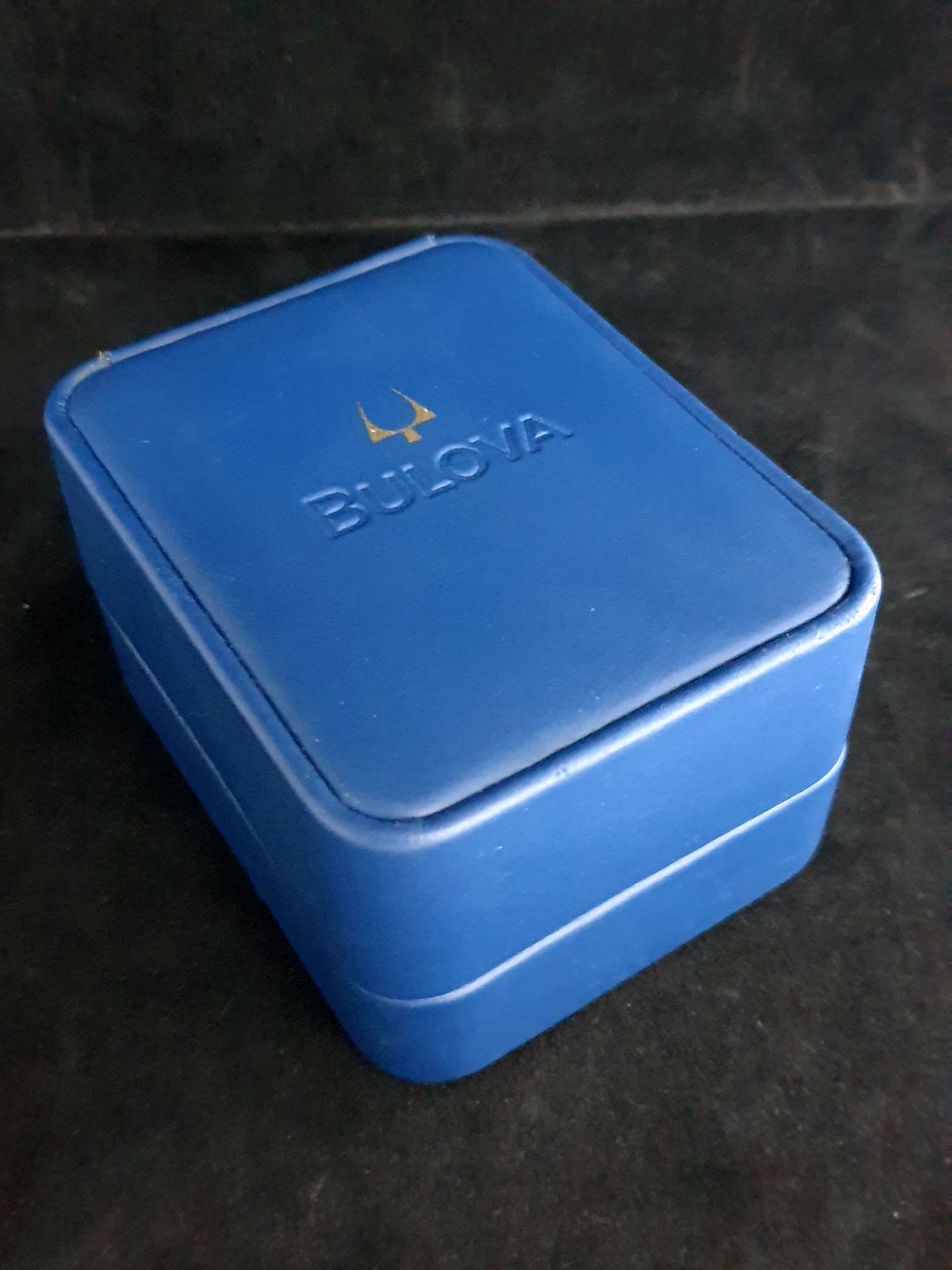 Blue rectangular lunchbox with a gold logo on a dark background