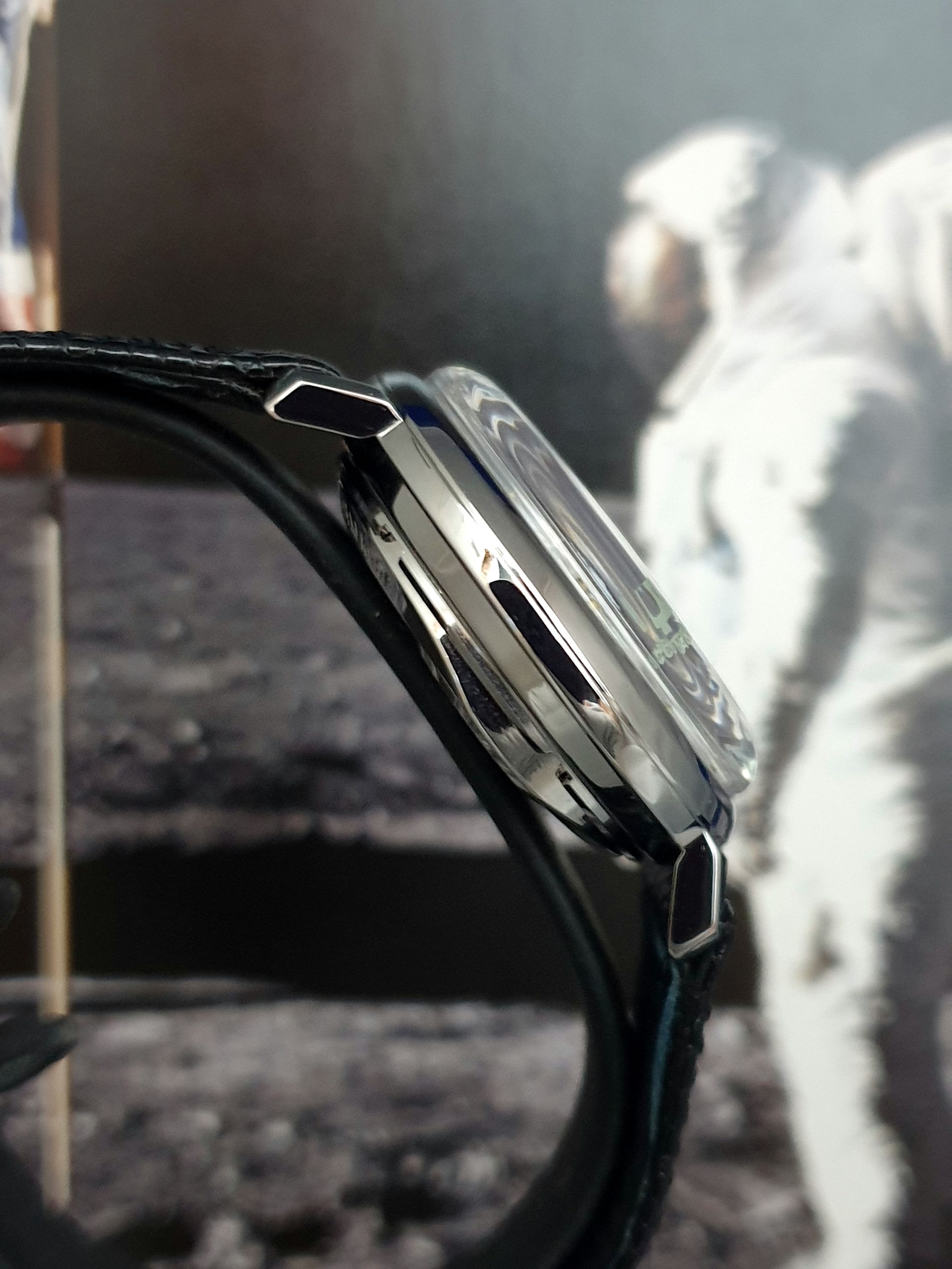 Close-up of a black wristwatch with a silver face against a blurred grayscale background