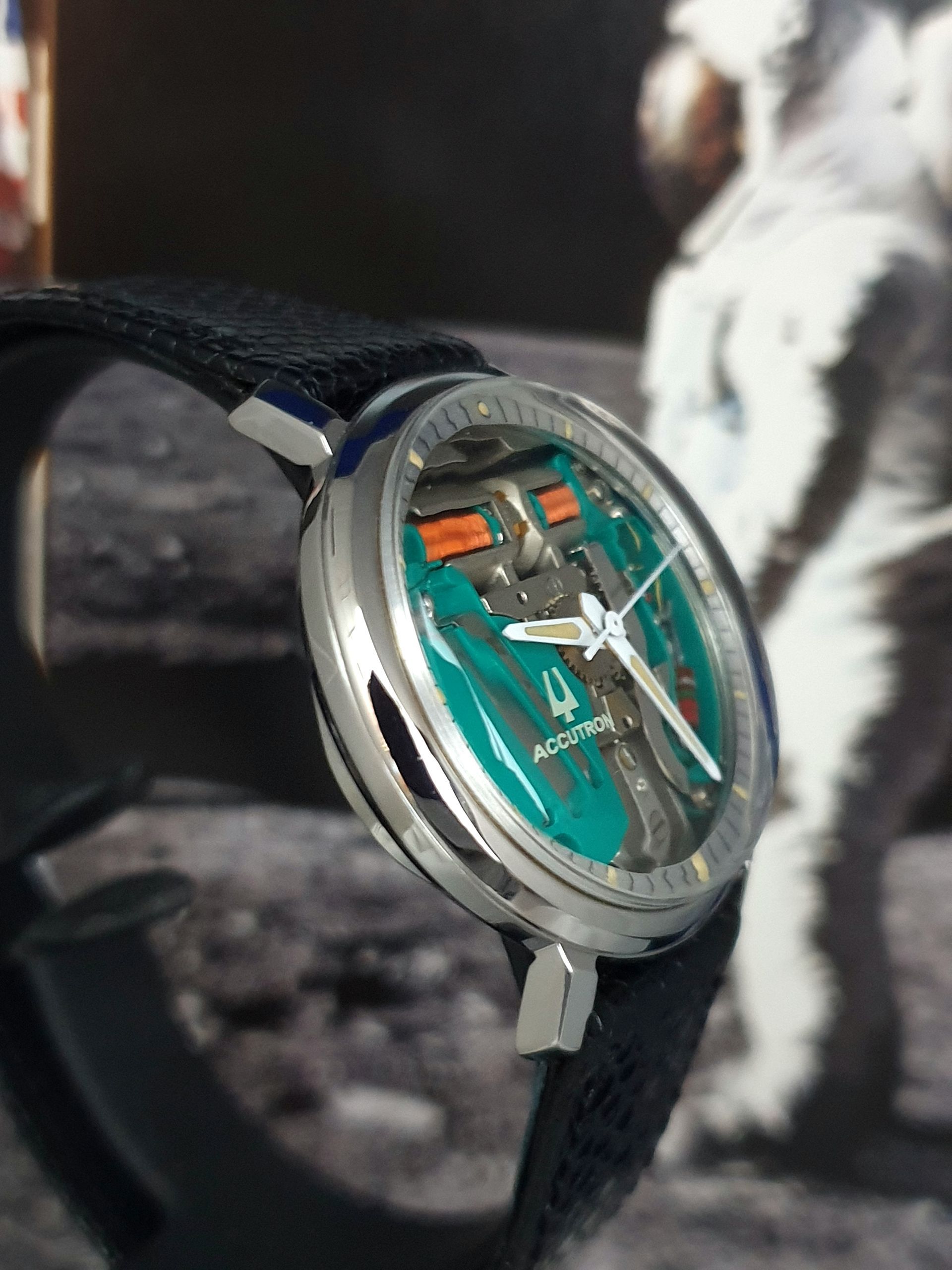 Close-up of a green-dial wristwatch with a black strap against a blurred black-and-white background