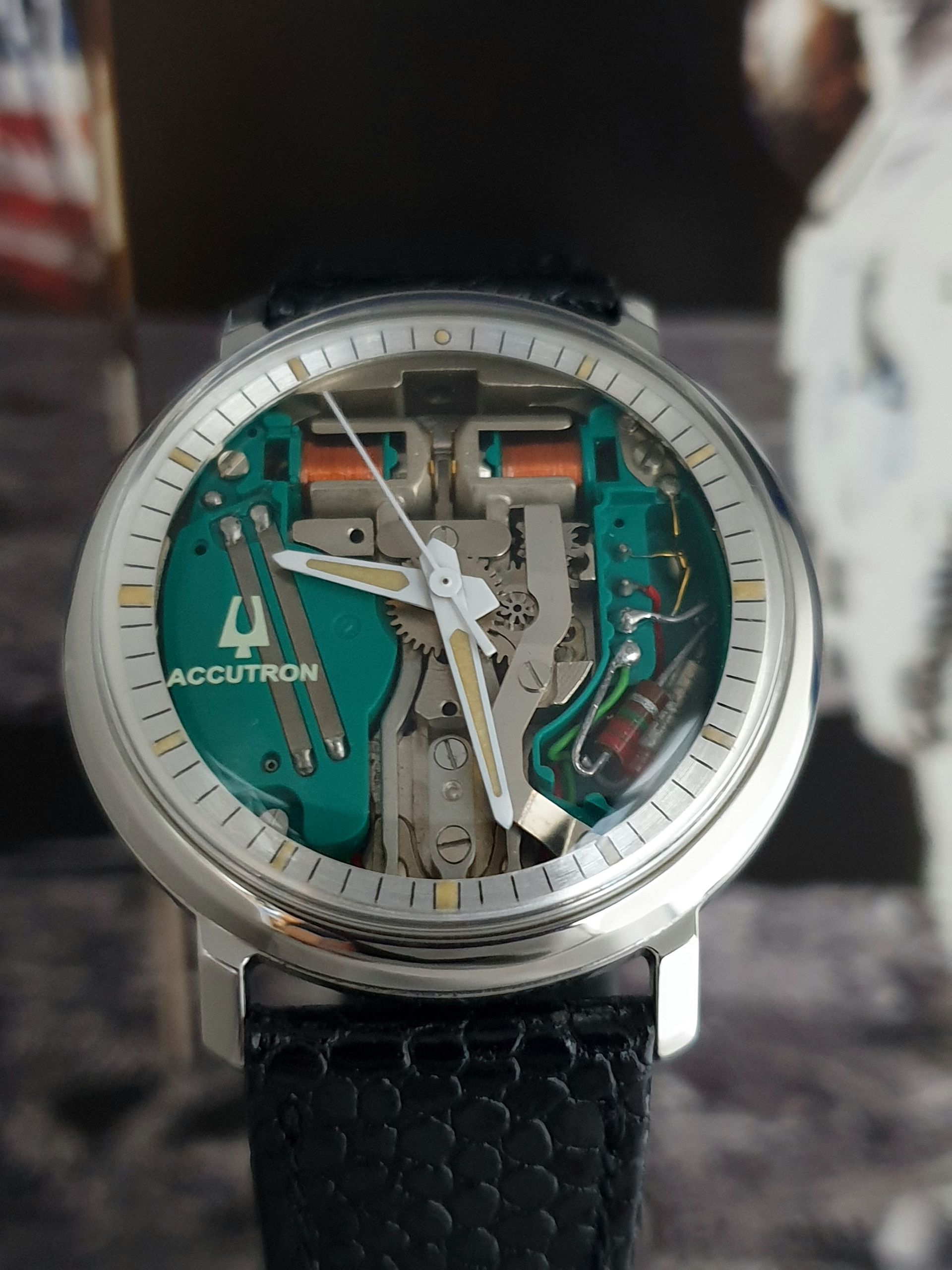 Close-up of a silver skeleton wristwatch with teal gears and a black leather strap